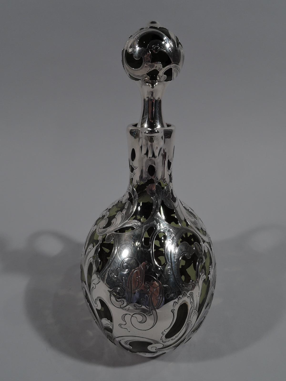 Turn-of-the-century Art Nouveau glass decanter with engraved silver overlay. Curved ovalish body with high looping reeded handle and cylindrical neck. Ball stopper. Overlay in form of loose and exuberant scrolls and flowers. On front asymmetrical