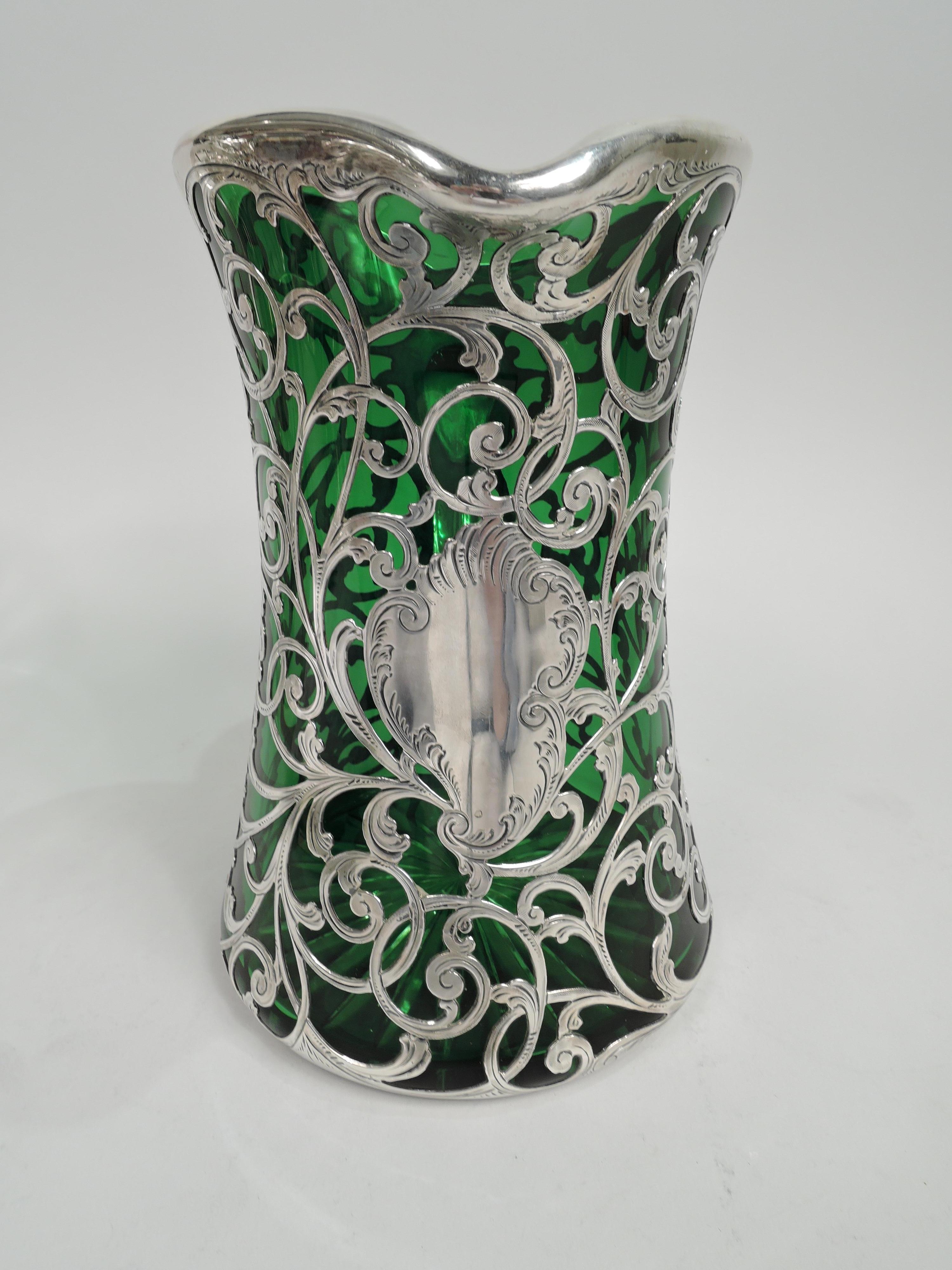 Turn-of-the-century Art Nouveau glass jug with engraved silver overlay. Made by Gorham in Providence. Waisted cylinder with scalloped mouth and small lip spout. Overlay in form of loose and entwined leafing scrollwork, and asymmetrical cartouche