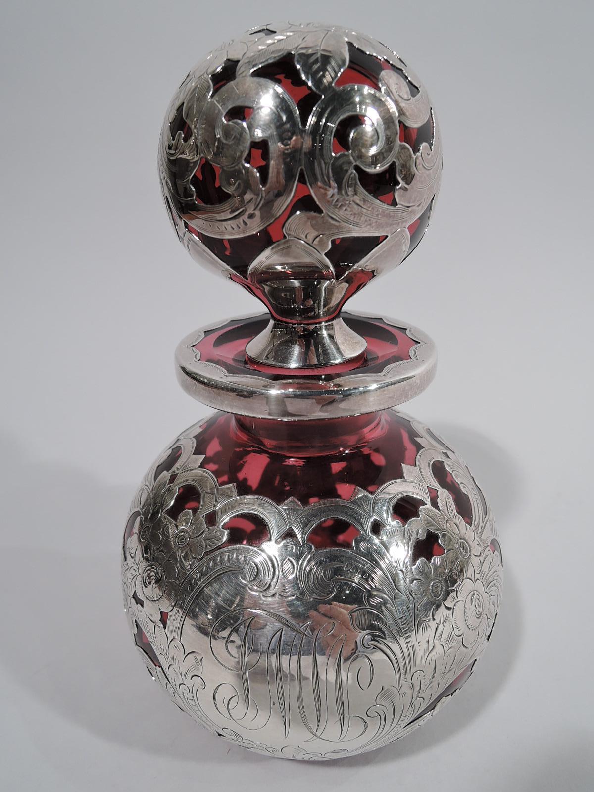 Art Nouveau red glass cologne bottle with engraved silver overlay. Made by Gorham in Providence, circa 1886. Globular with short neck and flat everted rim. Stopper globular. Tight and dense overlay with flower heads and rolling scrolls. Scalloped