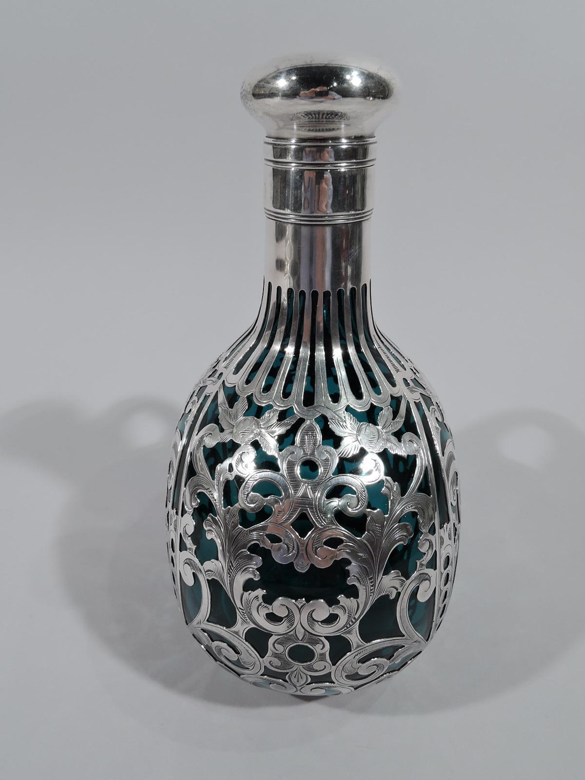 Art Nouveau glass decanter with silver overlay. Made by Gorham in Providence, ca 1890. Flattish round bowl with cylindrical neck and hinged and cork-lined cover. Glass is blue-tinged sea green (or teal) with dense overlay in form of leafy scrolls