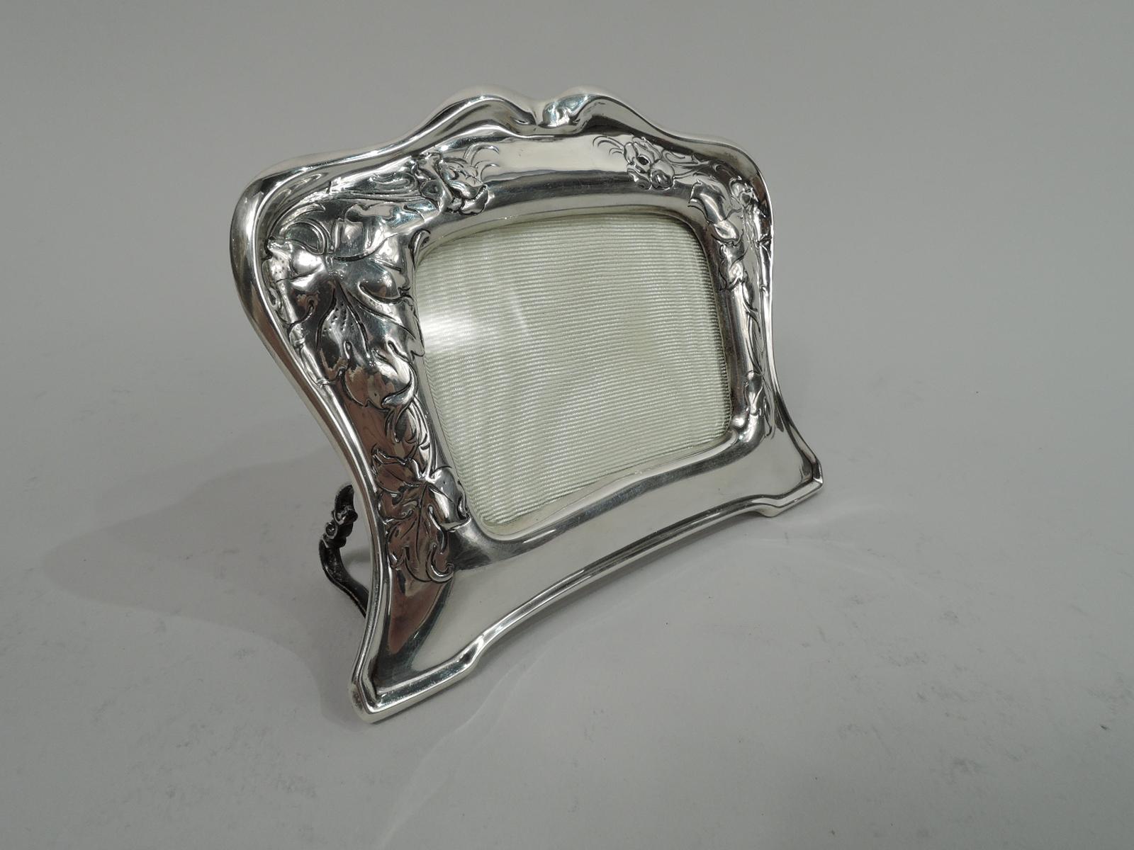 Art Nouveau sterling silver boudoir frame. Made by Gorham in Providence in 1902. Rectangular window in shaped surround with bracket feet and back-mounted scrolled loop supports. Fluid leaf and flowers chased and engraved on sides and top forming
