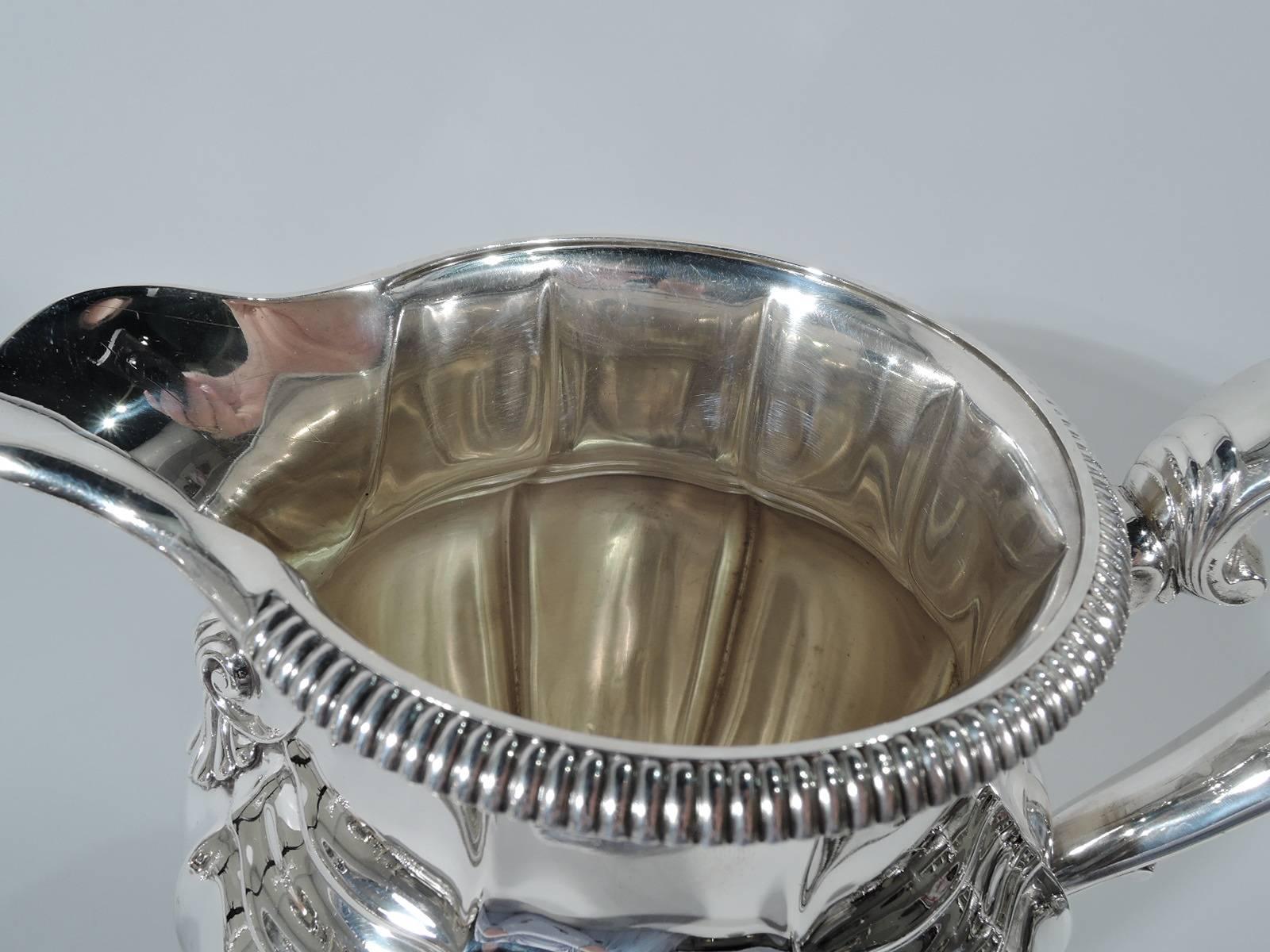 Classical sterling silver water pitcher. Made by Gorham in Providence, ca 1930. Lobed baluster with u-spout, capped scroll handle, and raised foot. Gadrooning. Volute scroll and scallop shell at spout base. Hallmark includes no. 531/1 and volume (4