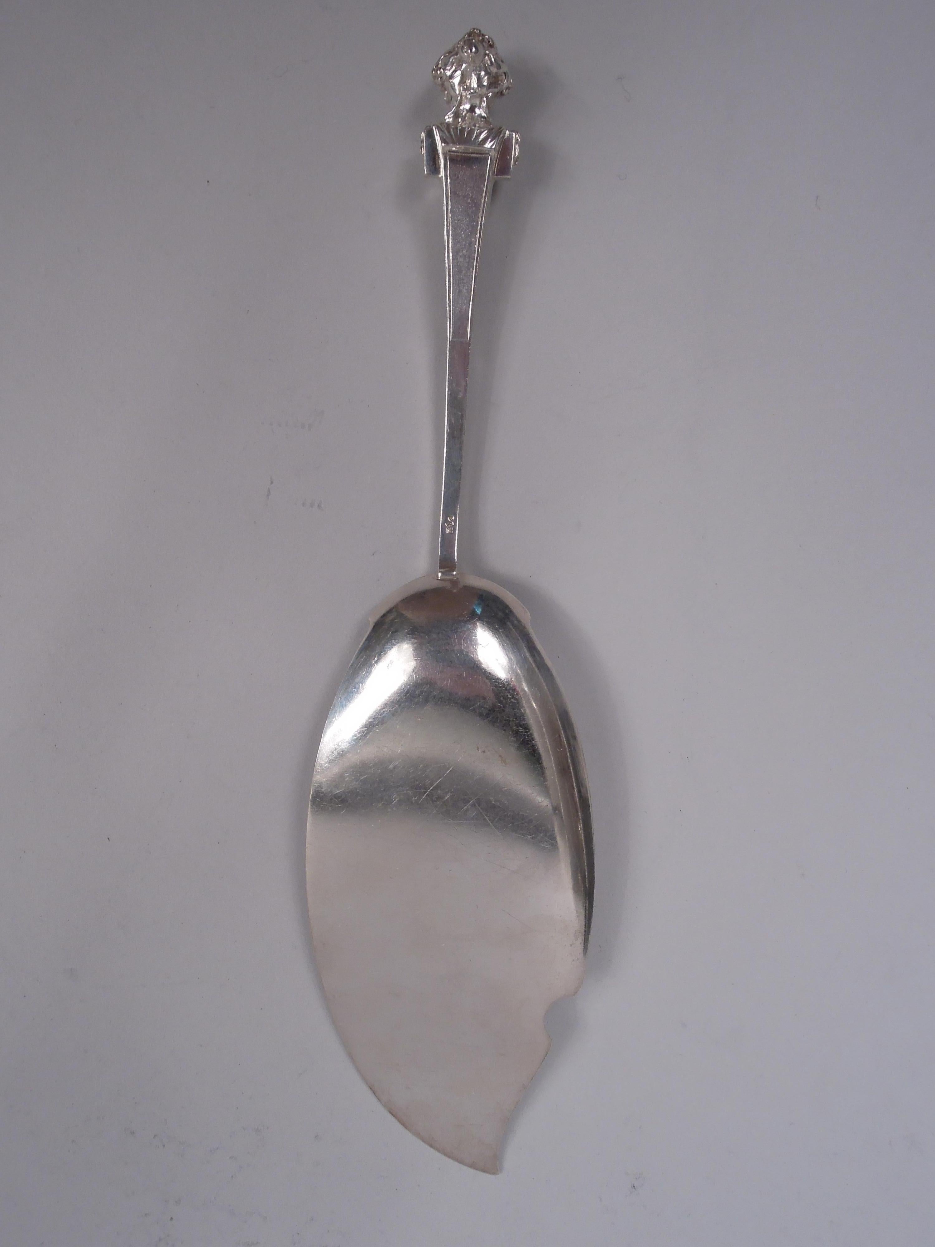 Bust coin silver fish slice. Made by Gorham in Providence, ca 1865. Flat shaped oval blade with stylized leaf and scroll ornament. Tapering rectilinear leaf-mounted handle with cast terminal in form of Classical matron. Maker’s mark. Weight: 5 troy