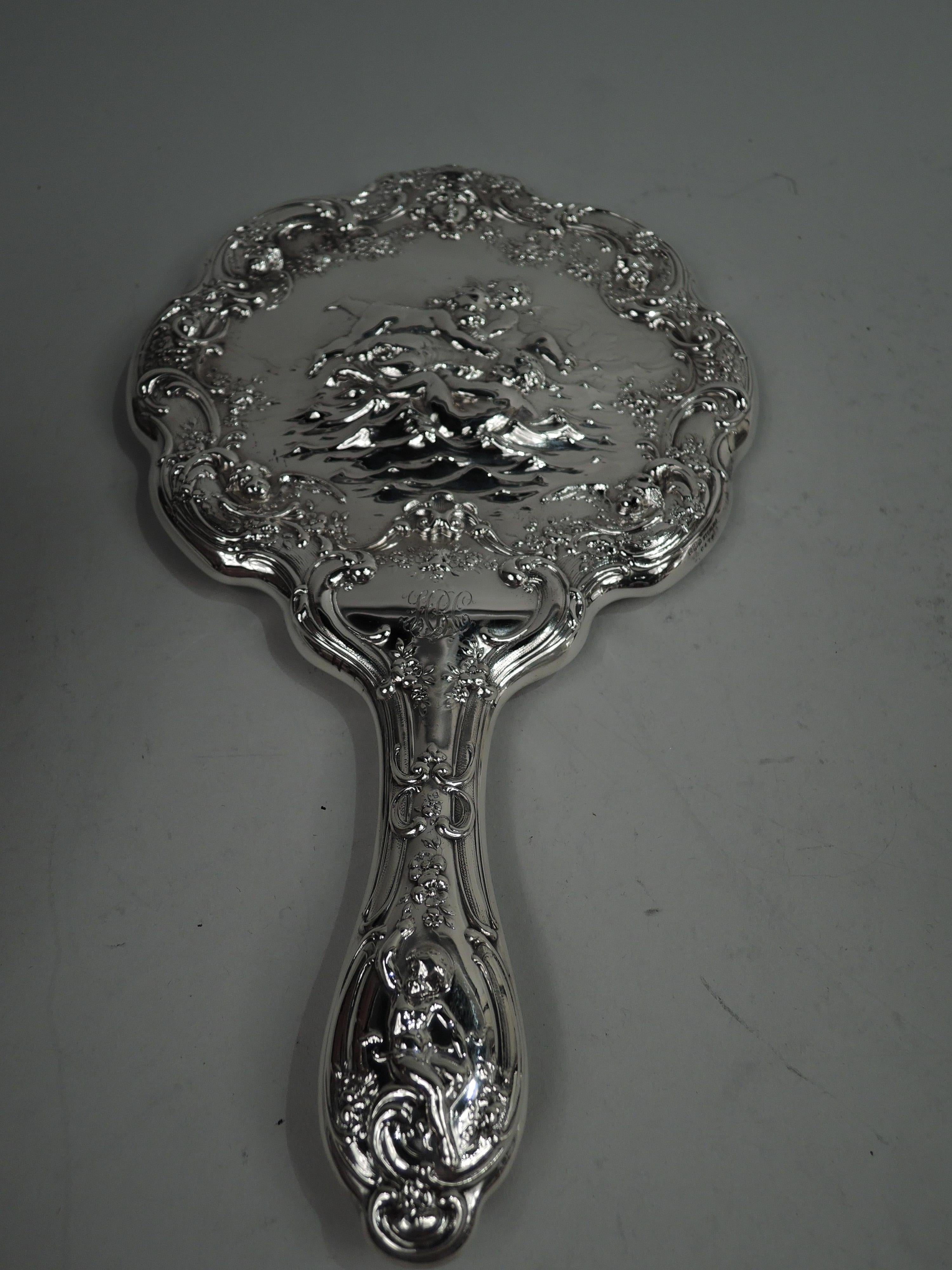 Edwardian Classical sterling silver vanity pair. Made by Gorham in Providence, ca 1900. This pair comprises hand mirror and hairbrush. Mirror has round scalloped frame and the brush has shaped oval frame. Embossed ornament with chubby, naked cherubs