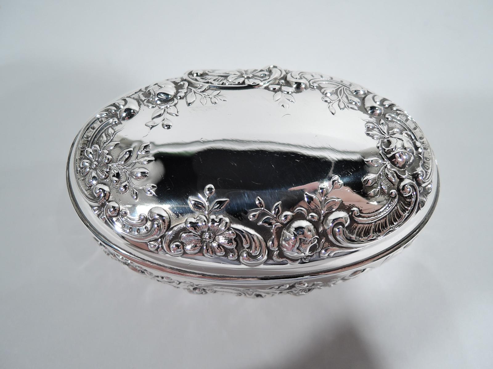 Edwardian Classical sterling silver trinket box. Made by Gorham in Providence, ca 1910. Oval with hinged and raised cover. Chased scroll and flower ornament. Cover top has vacant center. Interior gilt washed. Fully marked and numbered B160. Weight: