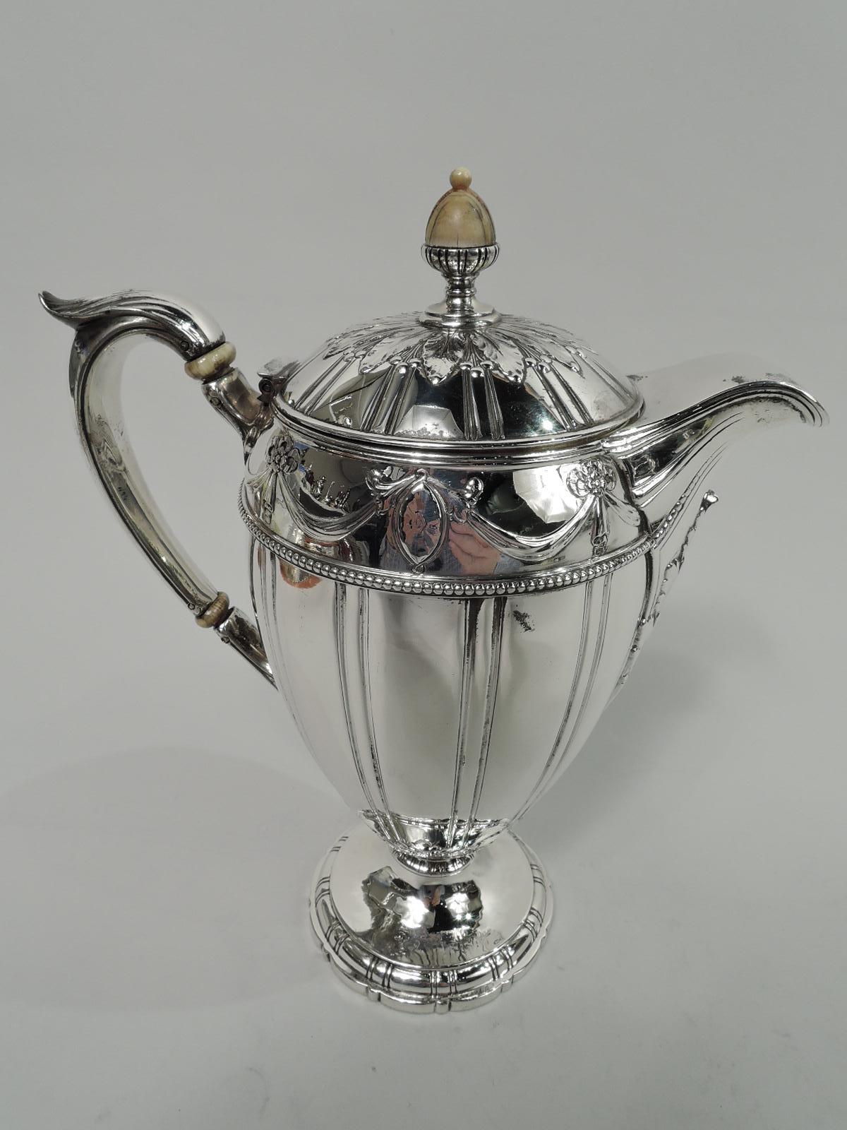 Edwardian Regency sterling silver coffeepot. Made by Gorham in Providence, ca 1910. Ovoid body, raised and hinged cover with acorn finial, leaf-capped high looping handle, and raised and scalloped foot. Pilasters, beading, and bead and reel. Leaf