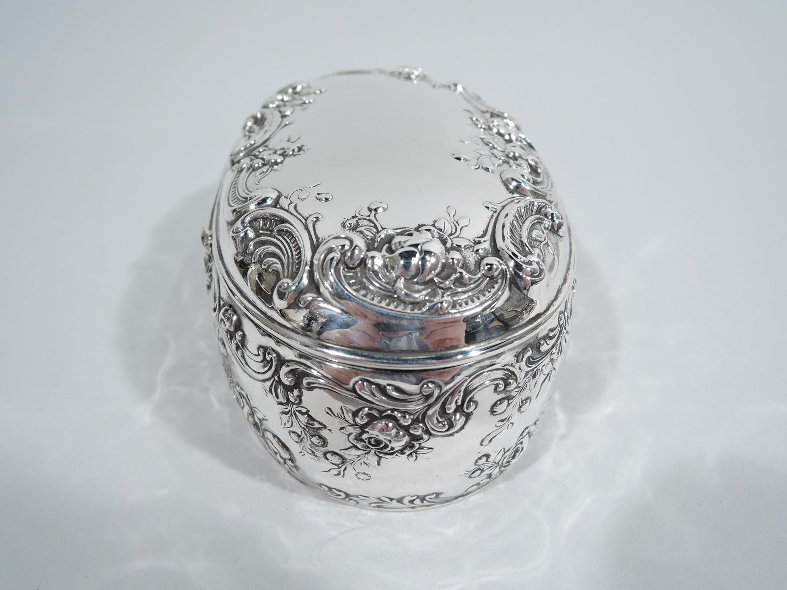 Turn-of-the-century Edwardian sterling silver jewelry box. Made by Gorham in Providence. Oval. Sides gently curved as is hinged cover. Pretty and lively ornament in form of chased scrolls and flowers. Cover top center vacant. Box interior has fitted