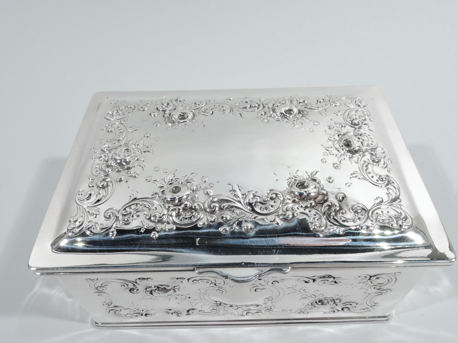 Edwardian sterling silver keepsake casket. Made by Gorham in Providence in 1899. Rectangular with straight sides. Cover hinged and gently raised with scrolled tab. Chased scrolls and flowers. Front has vacant scrolled cartouche. Cover top center