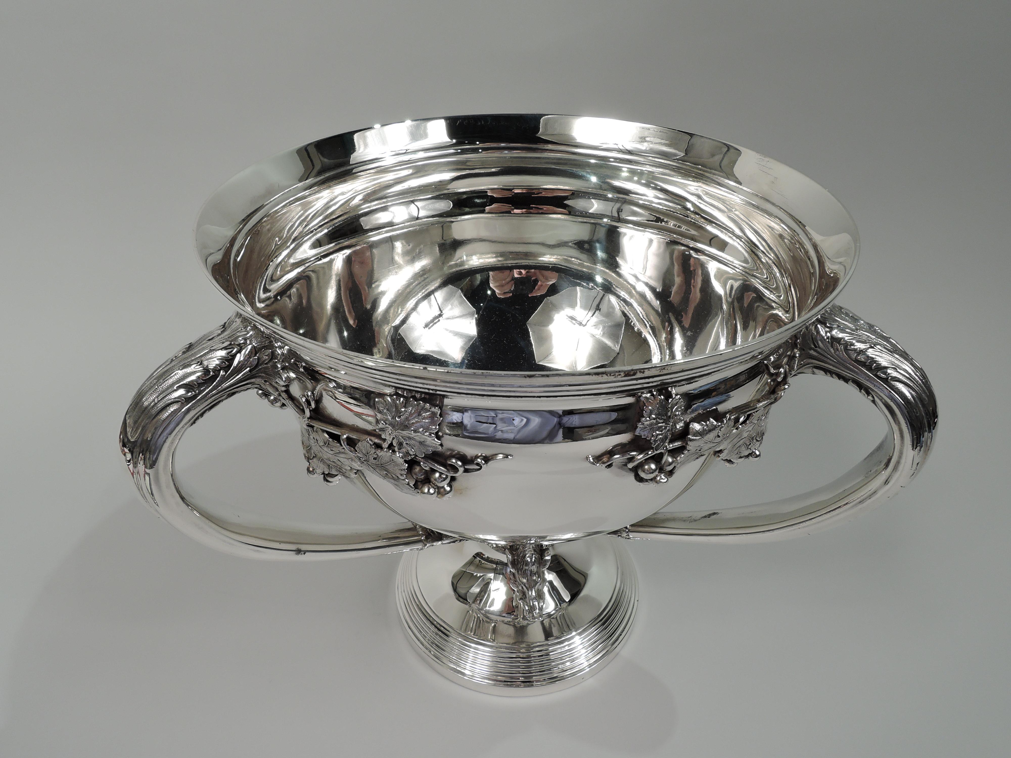 Gilded Age sterling silver loving cup. Made by Gorham in Providence, ca 1890. Round and tapering bowl with 3 handles leaf-mounted to bowl and knop. Flared rim and raised foot; both with stepped reeding. Meandering fruiting grapevine with curlicue