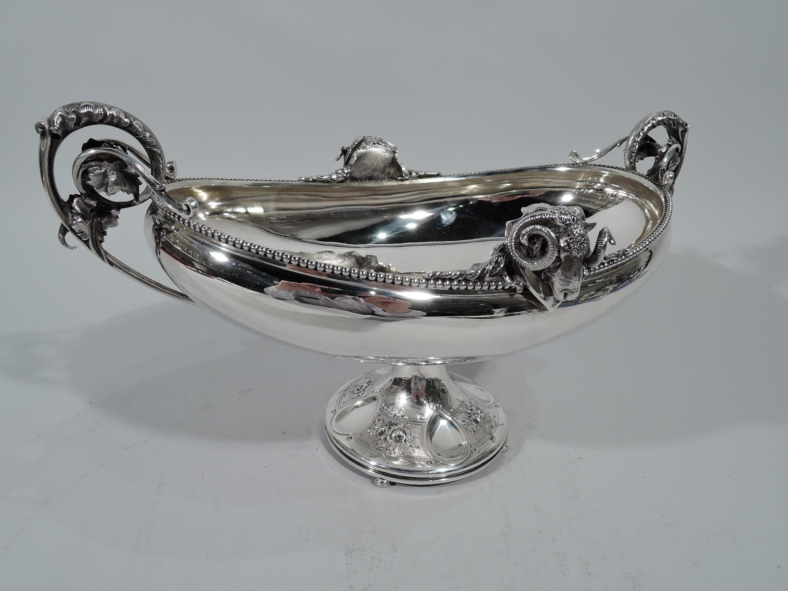 Greek Revival coin silver footed bowl. Made by Gorham in Providence, circa 1860. Oval bowl with foliate volute scroll end handles. Rim beaded with applied cast ram’s heads. Conical foot with beaded knop and four beaded disc supports. Foot has