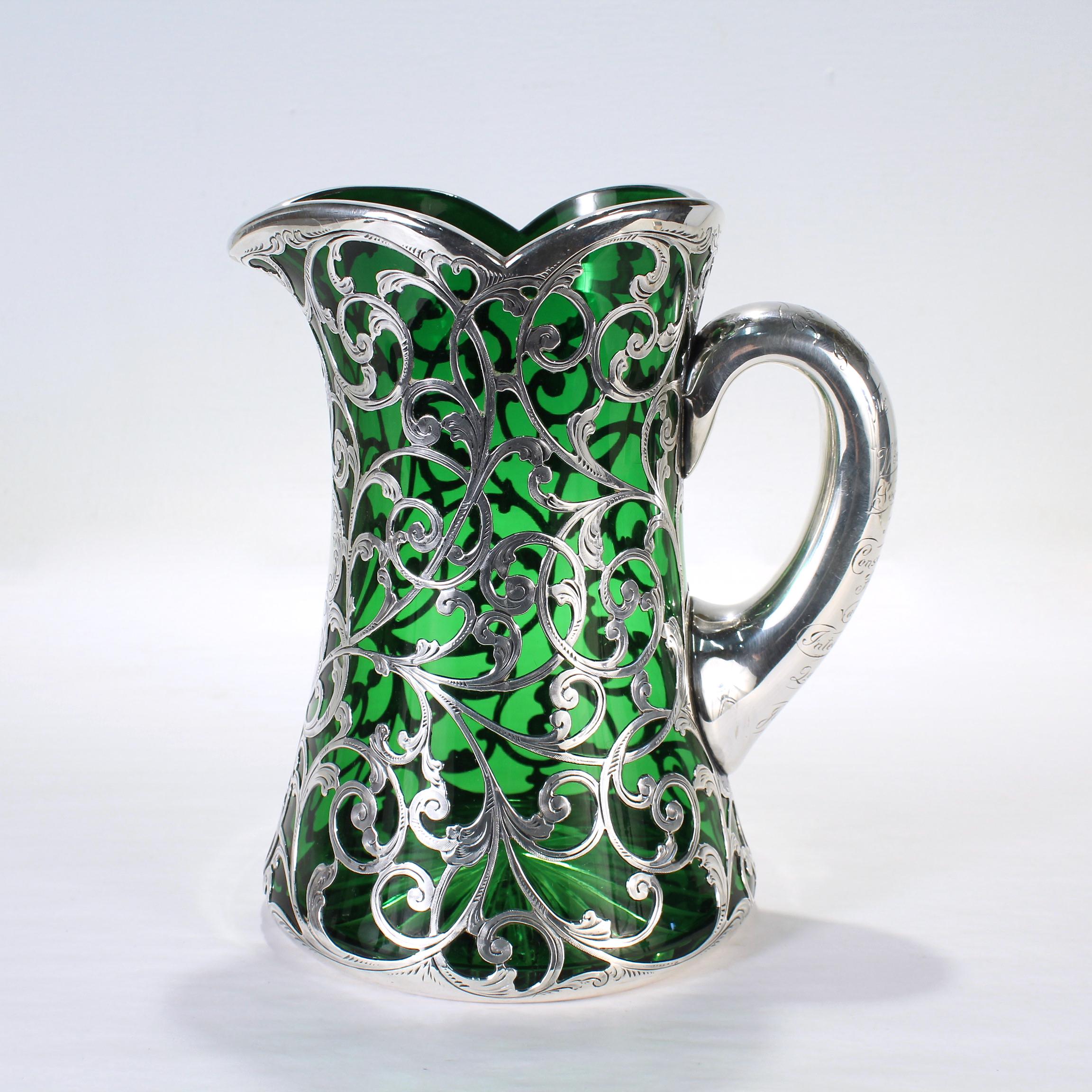 A fine antique silver overlay green glass pitcher.

By Gorham.

Decorated throughout with an ornate heavy-gauged silver overlay. 

Engraved to the handle: 