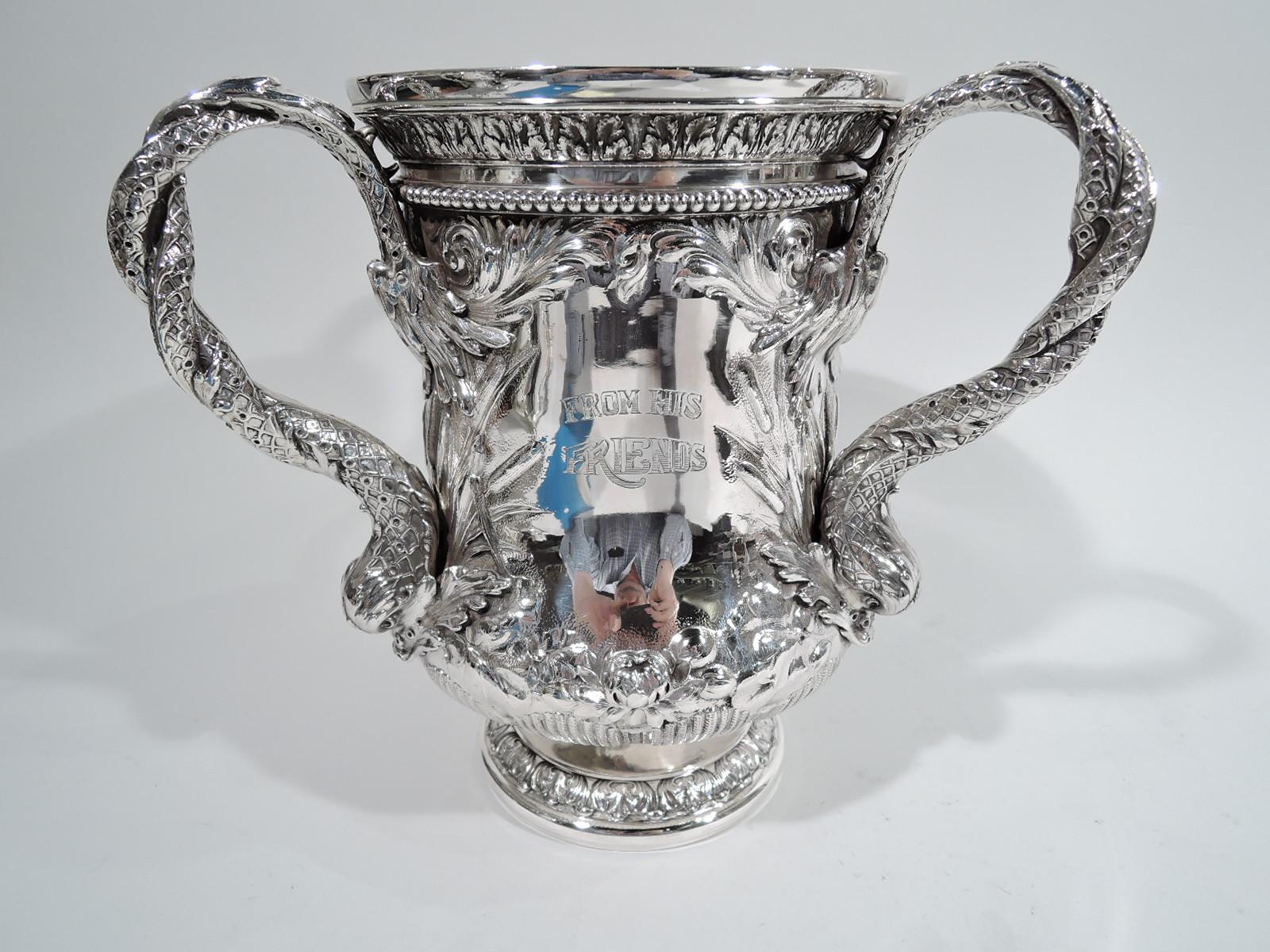 Victorian Classical sterling silver loving cup. Made by Gorham in Providence in 1893. Bellied urn with 3 twisted and scaly dolphin handles and raised and round foot. Interior richly gilt.

Three-sided presentation framed by dense and exuberant