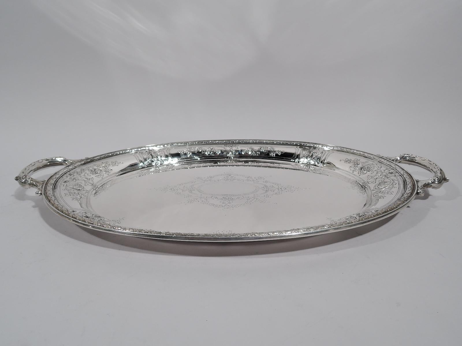 Maintenon sterling silver serving tray. Made by Gorham in Providence in 1925. Oval with leaf-capped and-mounted c-scroll side handles. Well has engraved beaded oval frame (vacant) surrounded by garlands and pendant flowers. Tapering shoulder with