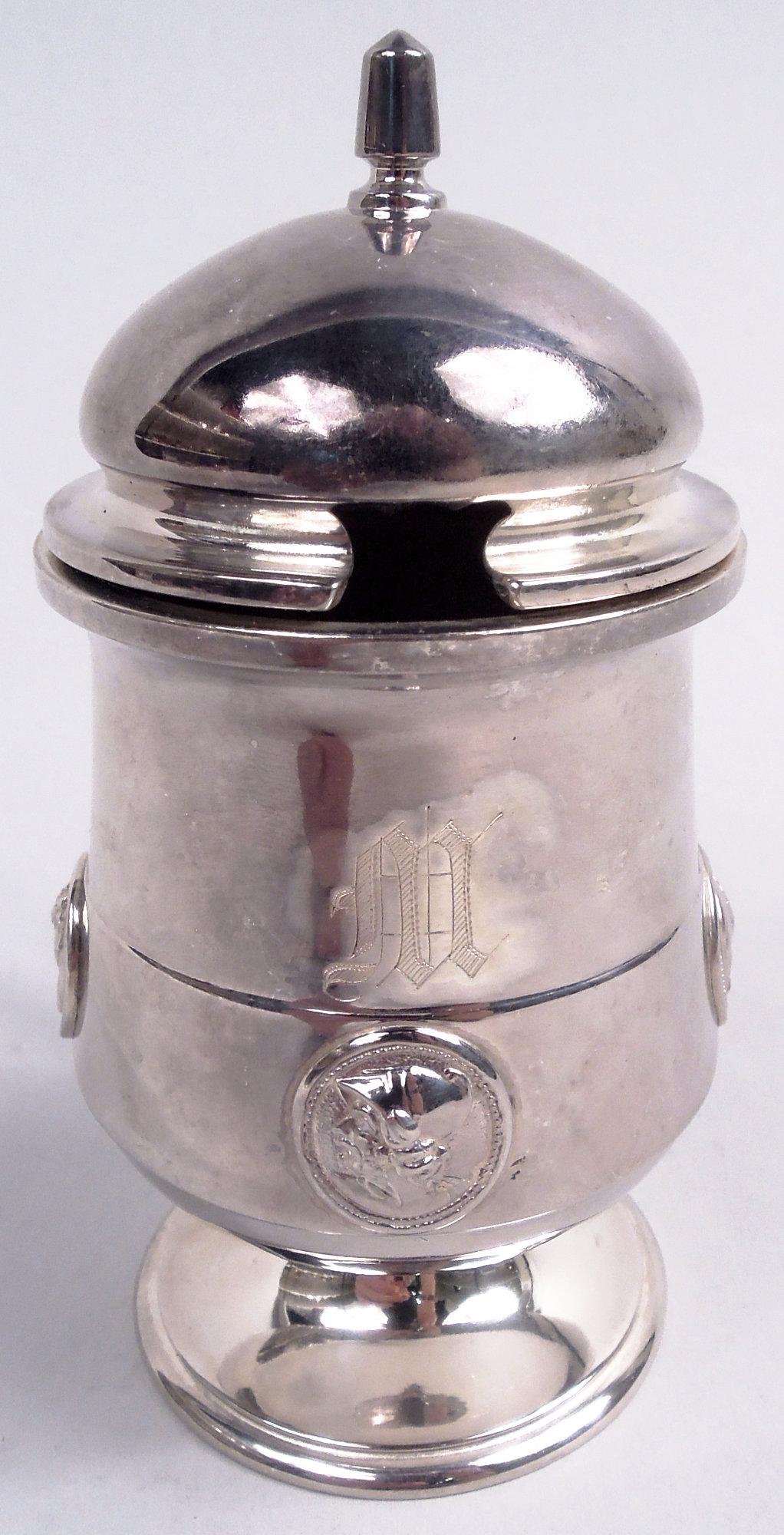 Vasetto di senape in argento con medaglione. Prodotto da Gorham a Providence, nel 1860 circa. Ciotola affusolata verso l'alto su piede rialzato. Coperchio incernierato e bombato e maniglia a staffa con volute di foglie. Fascia piatta con 3 profili