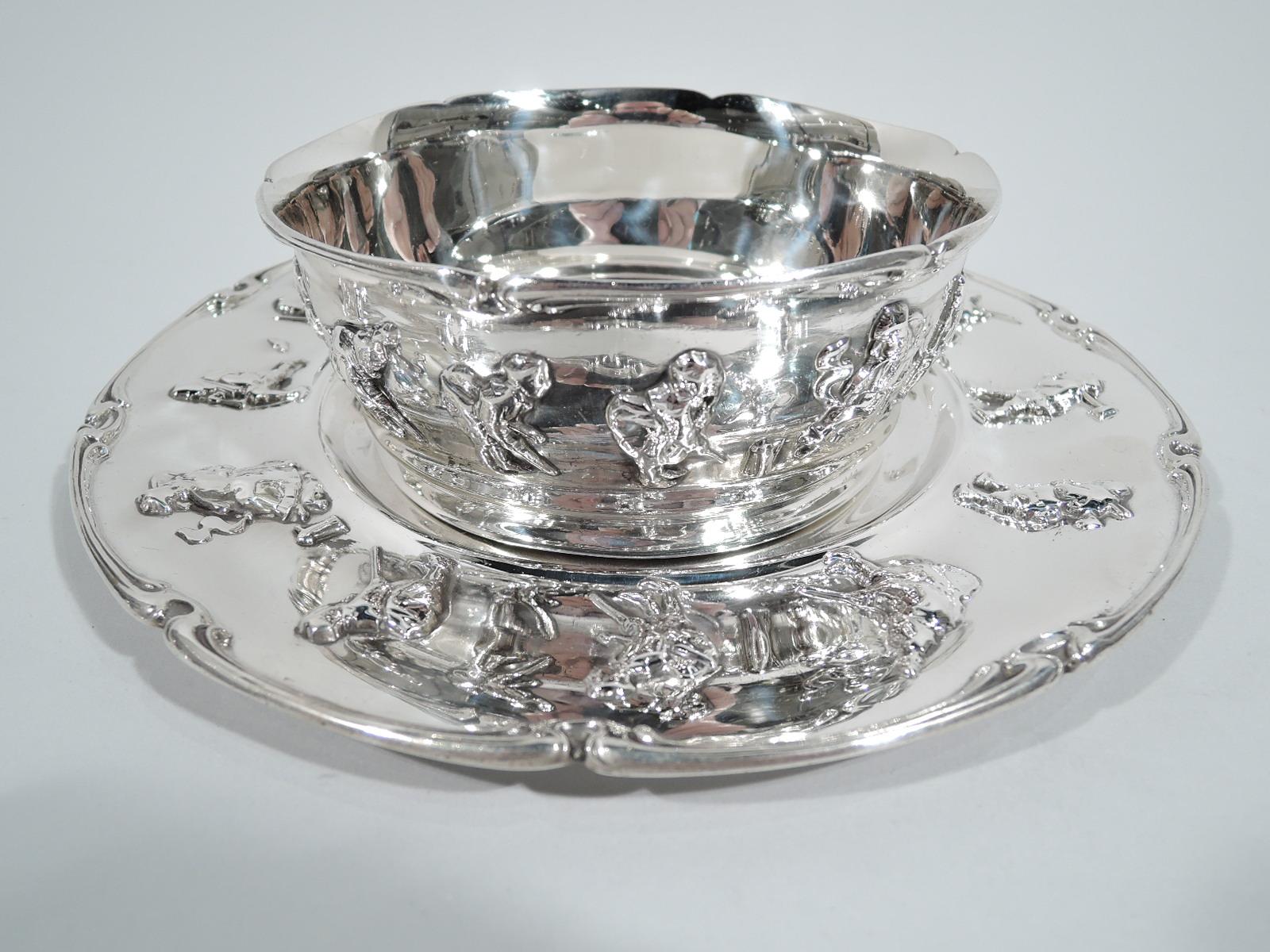 Edwardian sterling silver baby bowl on plate. Made by Gorham in Providence in 1911. Bowl has curved and tapering sides. Plate has well and wide shoulder. Both have whiplash-scrolled rim and applied figures—an eclectic frieze that includes