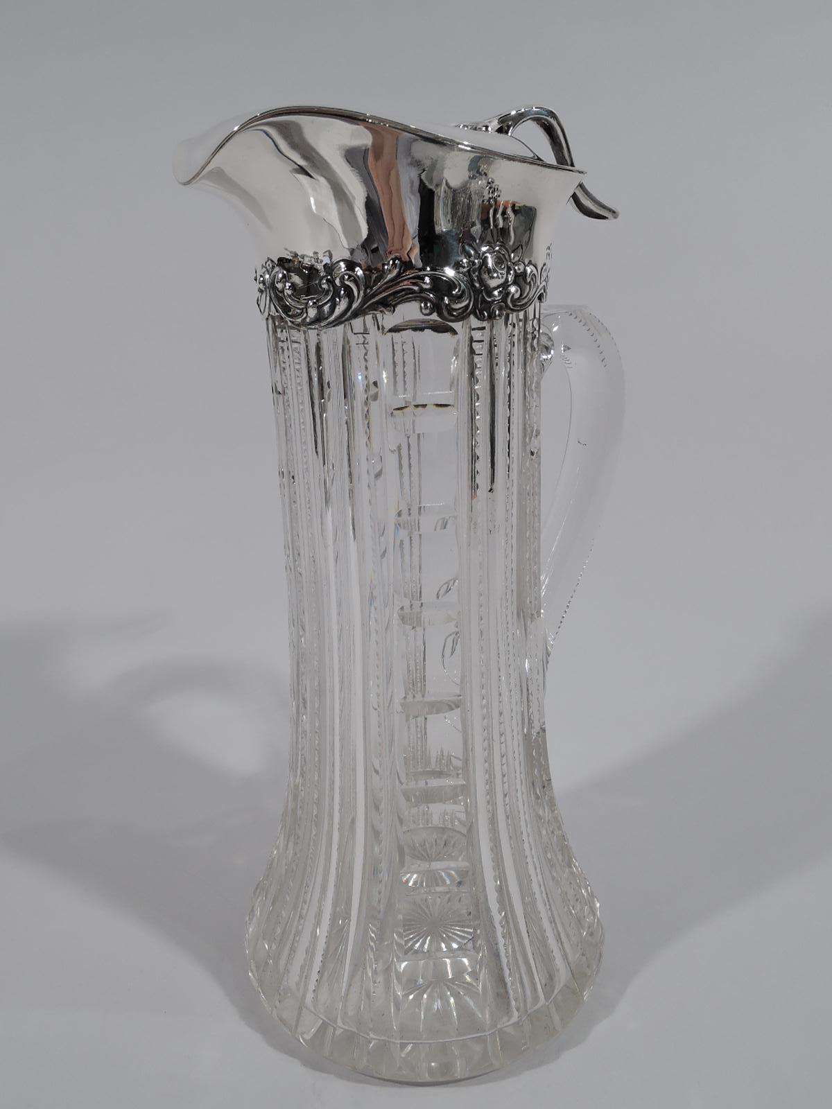 Turn-of-the-century brilliant-cut glass claret jug with sterling silver mount. Made by Gorham in Providence. Cylindrical with spread base and high-looping handle. Vertical ornament with flutes, notches, and stylized egg-and-dart. Sterling silver