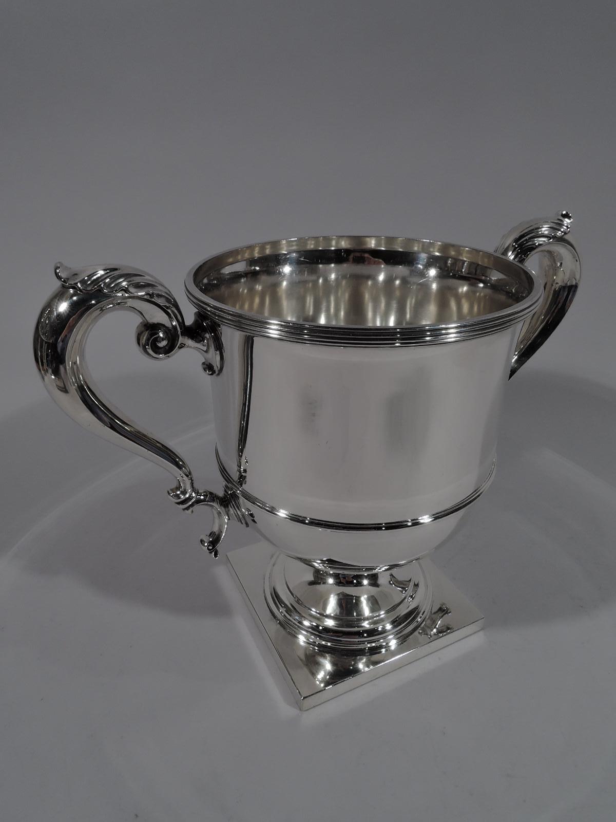 Classical sterling silver trophy. Made by Durgin (a division of Gorham) in Concord, New Hampshire, circa 1910. Girdled urn with reeded rim, leaf-capped double-scroll side handles, and stepped foot mounted to square base. The traditional form that is