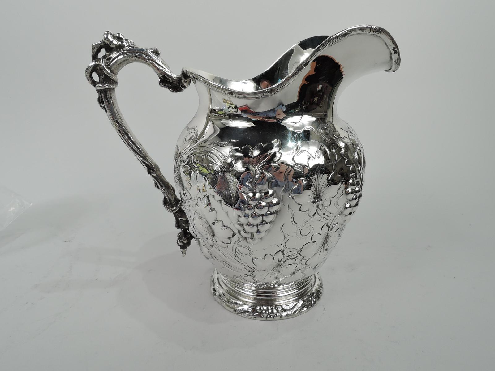 Turn-of-the-century sterling silver water pitcher. Made by Gorham in Providence. Ovoid body with helmet mouth and raised foot. High-looping vine handle. Chased fruiting grapevine and irregular frame (vacant). Fully marked including maker’s stamp and