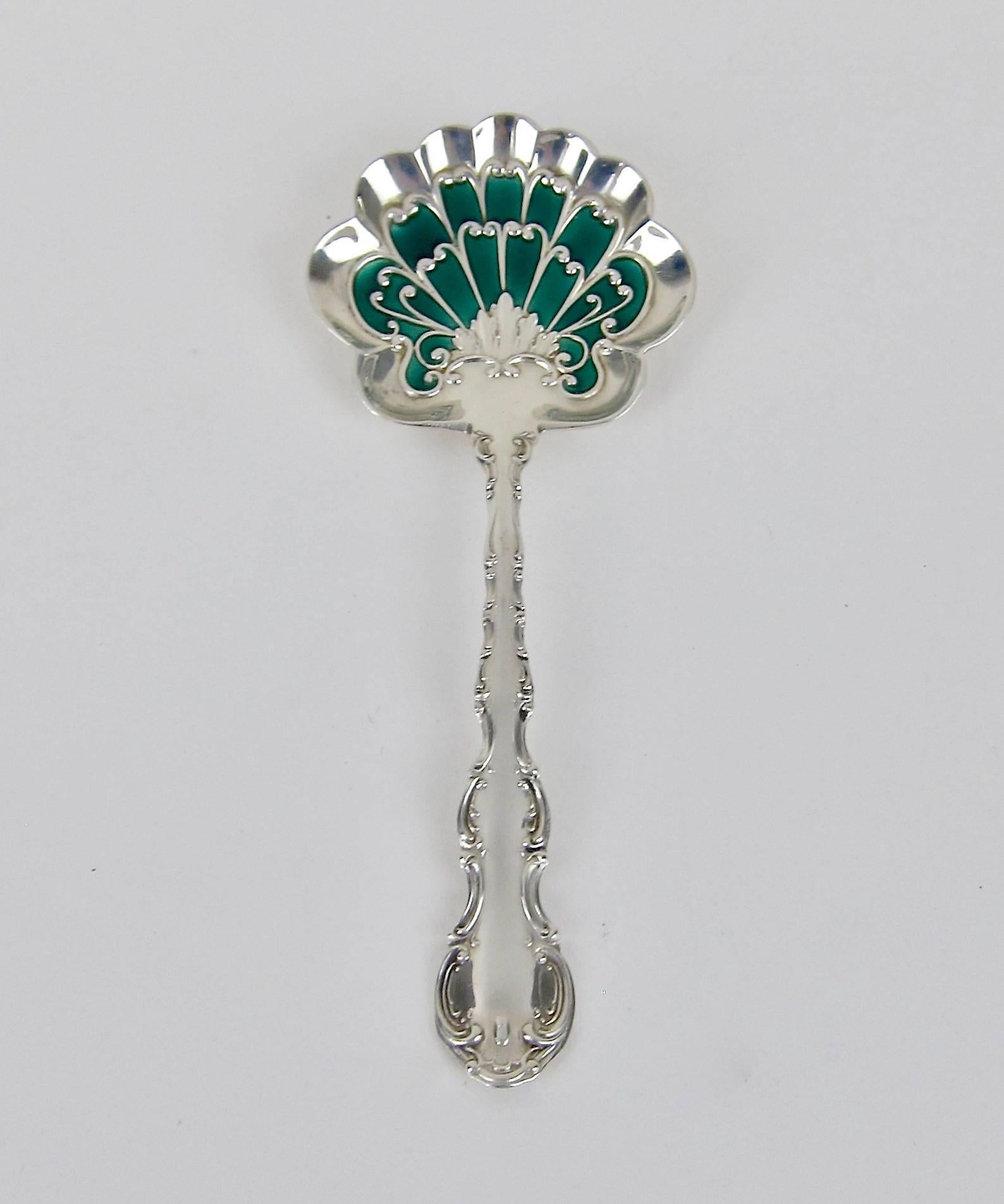 An antique bon bon spoon in solid sterling silver with contrasting enamel decoration of bright green from Gorham Manufacturing Company of Providence, Rhode Island. The spoon is from the company's Strasbourg pattern featuring scalloped edges,