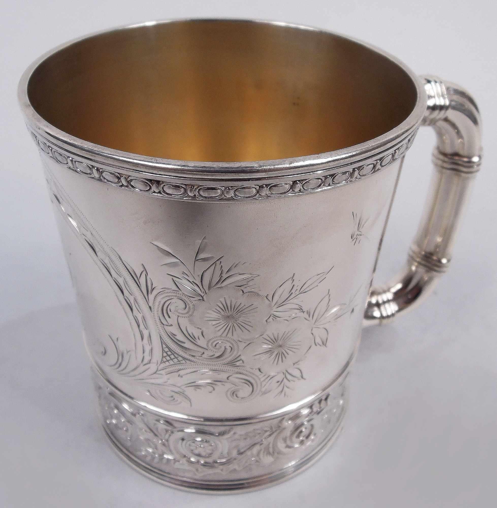 Victorian Classical sterling silver baby cup. Made by Gorham in Providence in 1888. Straight sides and lobed bracket handle with reeded bands. Stylized ornament: Scrolled frame surrounded by scrolls, leaves, flowers, and a couple hovering insects.