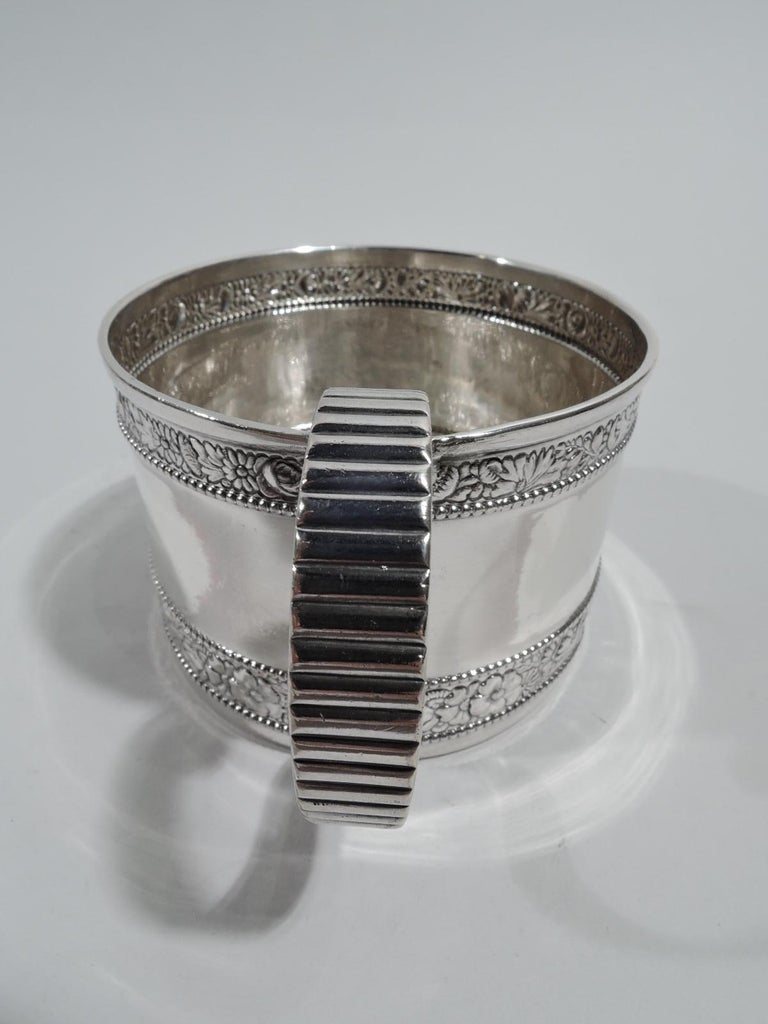 Victorian Classical sterling silver baby cup. Made by Gorham in Providence in 1890. Straight sides and ribbed scroll handle. Top and bottom have floral repousse bands between repousse borders. Fully marked including maker’s stamp, date symbol, and