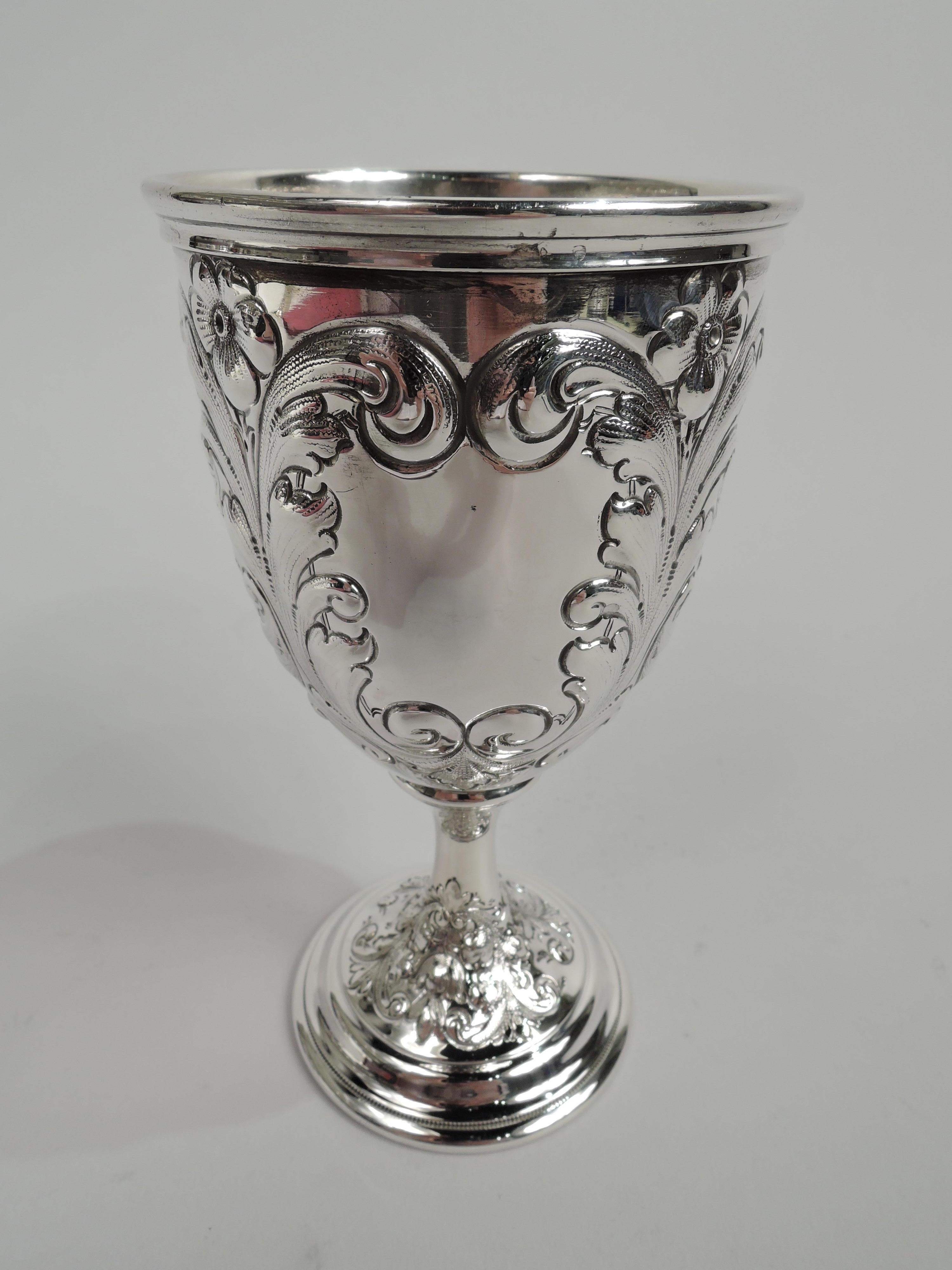 Victorian sterling silver goblet. Made by Gorham in Providence in 1892. Curved and tapering bowl, cylindrical stem, and stepped foot. Bowl has four leafing scroll frames of which two inset with flowers and one engraved with interlaced script