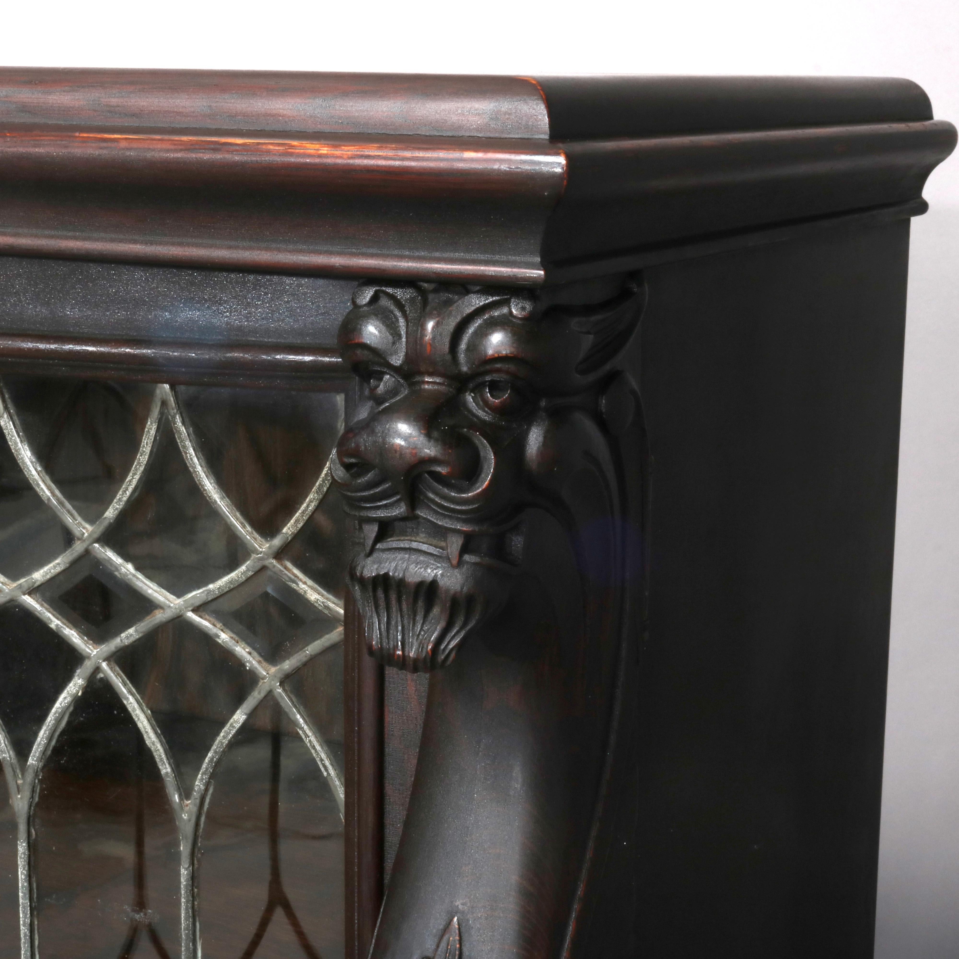 An antique Gothic figural bookcase offers oak construction with three leaded glass doors opening to shelved interior and having flanking carved griffins, raised on carved paw feet, circa 1890.

Measures - 56