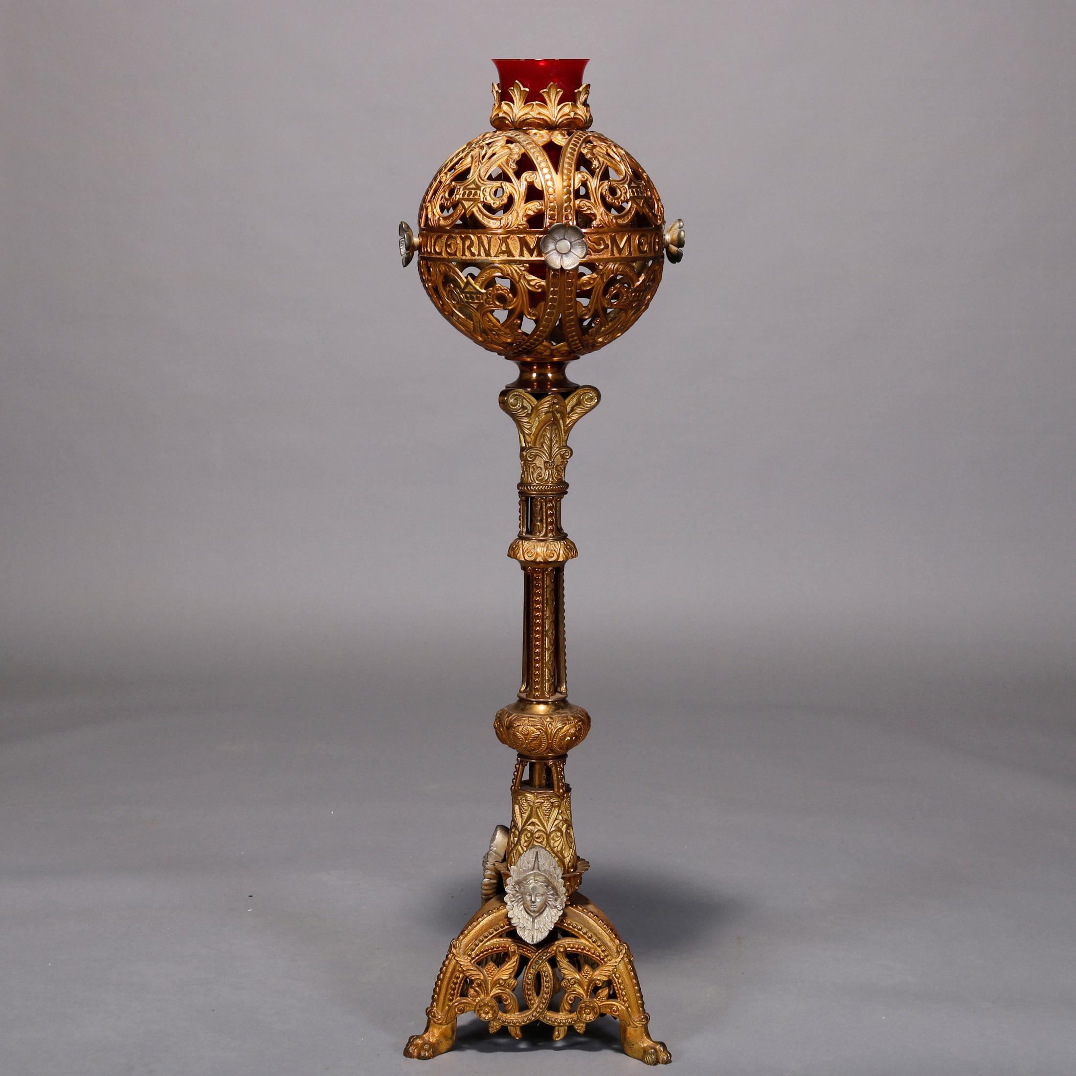 An antique Roman Catholic Gothic monstrance offers gilt bronze construction with pierced globe having scroll and foliate elements and housing ruby glass candle receptacle, surmounting ornate column raised on base with three legs with masks, foliate