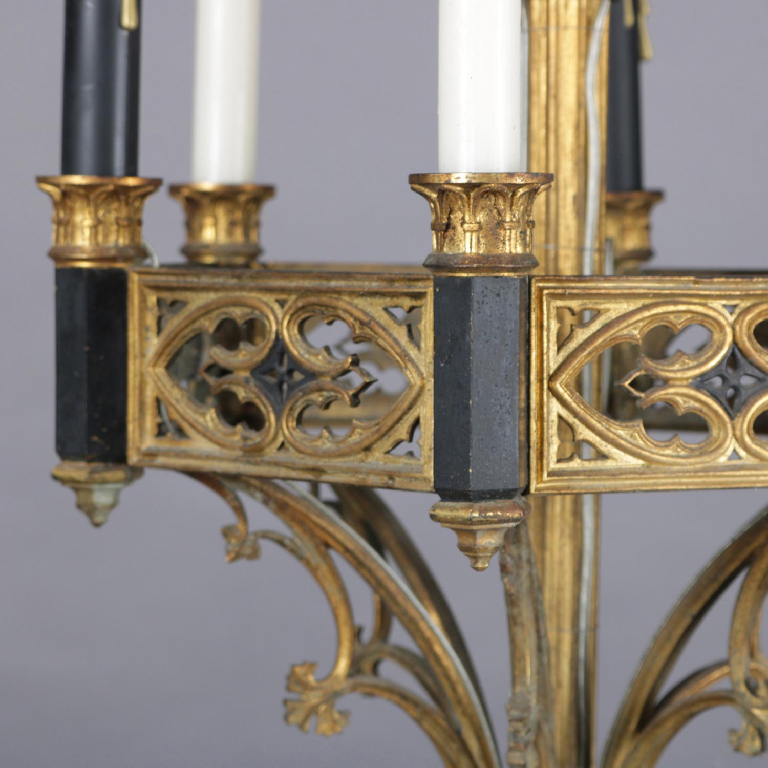 An antique Gothic style combination chandelier features ebonized and gilt metal reticulated frame having three electric candle lights and three wax candle sockets surmounting scroll form supports terminating in central drop finial, 20th