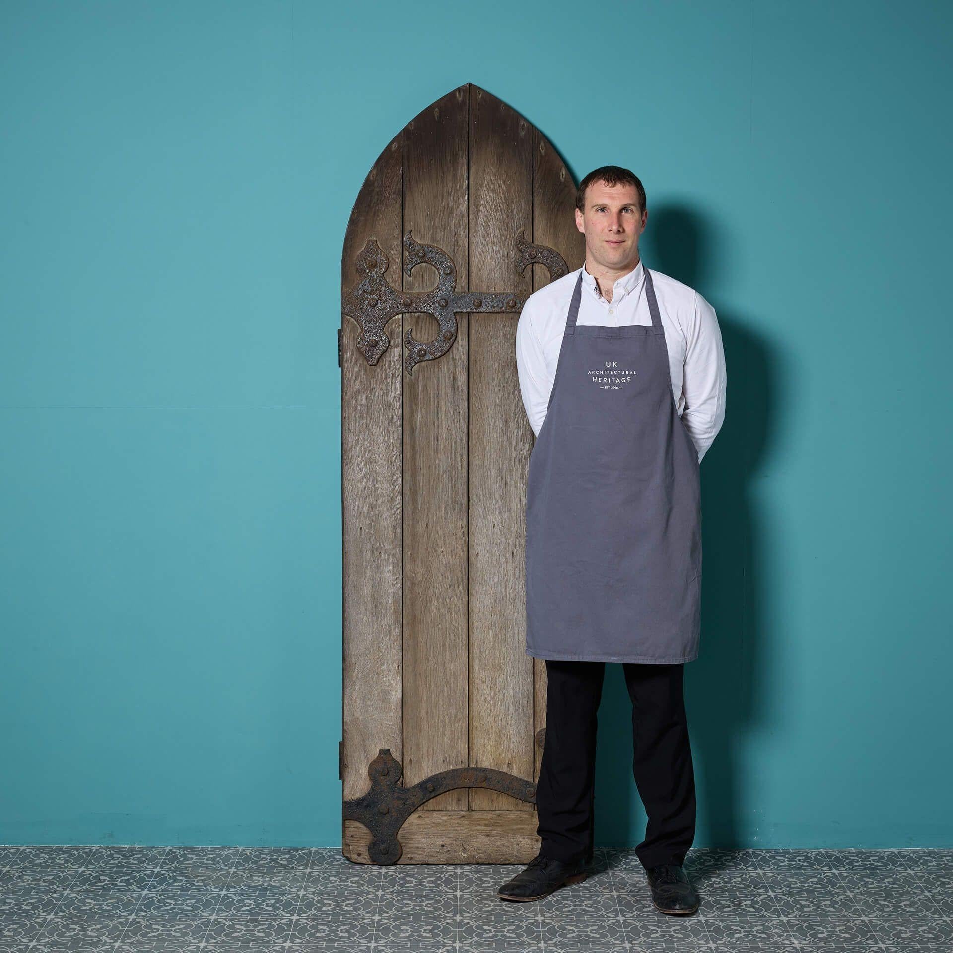 An enchanting tall arched oak door replicating something out of an ancient castle or English church.

Beautifully weathered by the ages and displaying ornate iron hinge embellishments to the front, this door dates from the late 19th century and