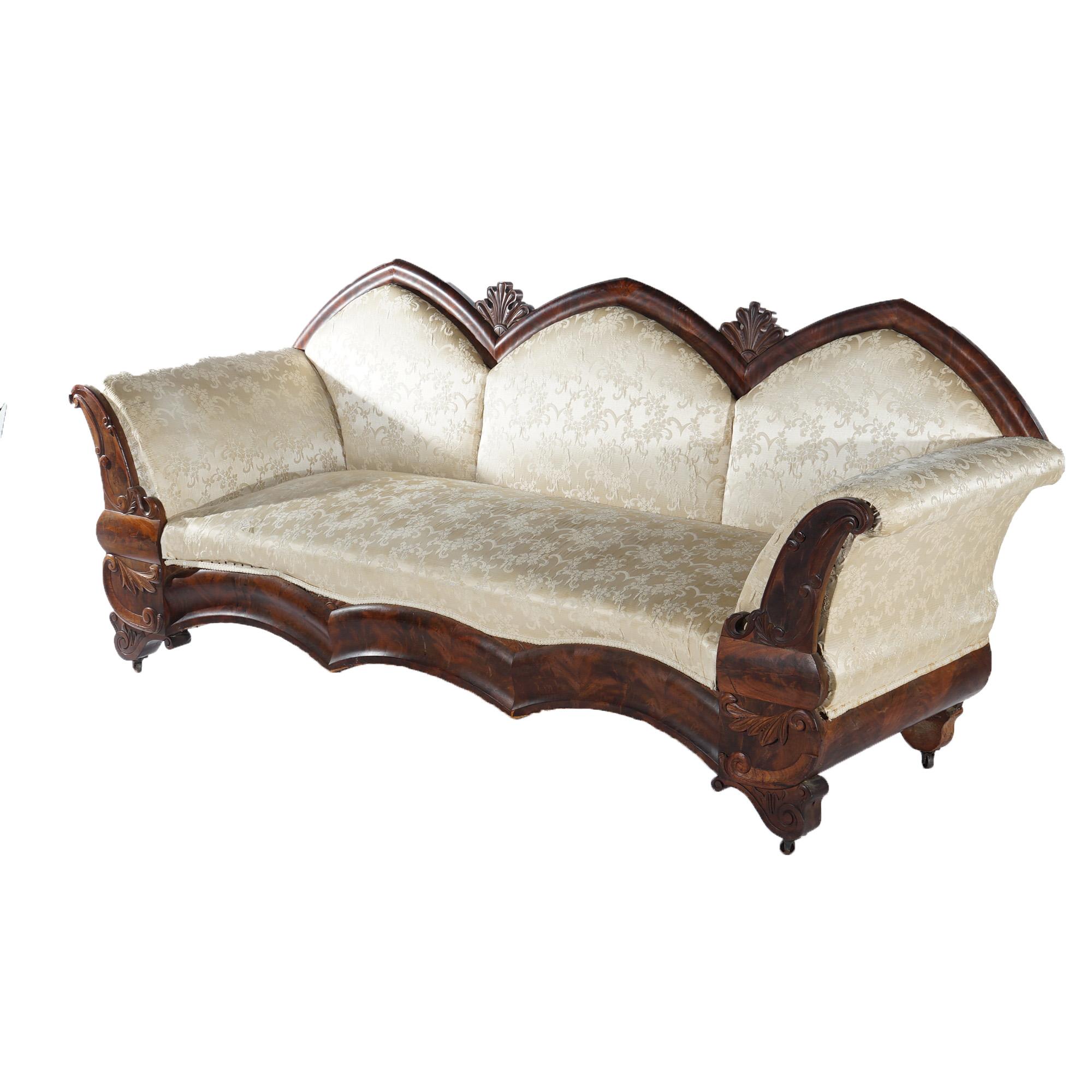 An antique Gothic Revival Classical sofa offers flame mahogany frame with triple cathedral form back, scroll form arms, carved foliate elements and raised on stylized scroll form feet; upholstered; c1850

Measures - 37