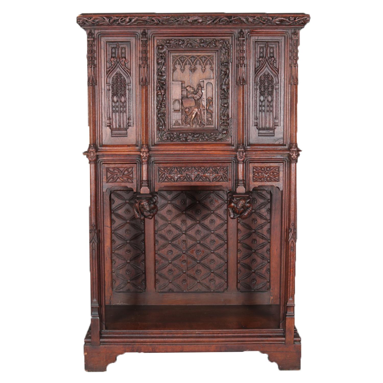 An antique Gothic Revival oak cabinet features upper with central door having heavily carved pictorial scene depicting monk priest in study, flanked by panels with cathedral arch design surmounting three drawers having foliate design with figural