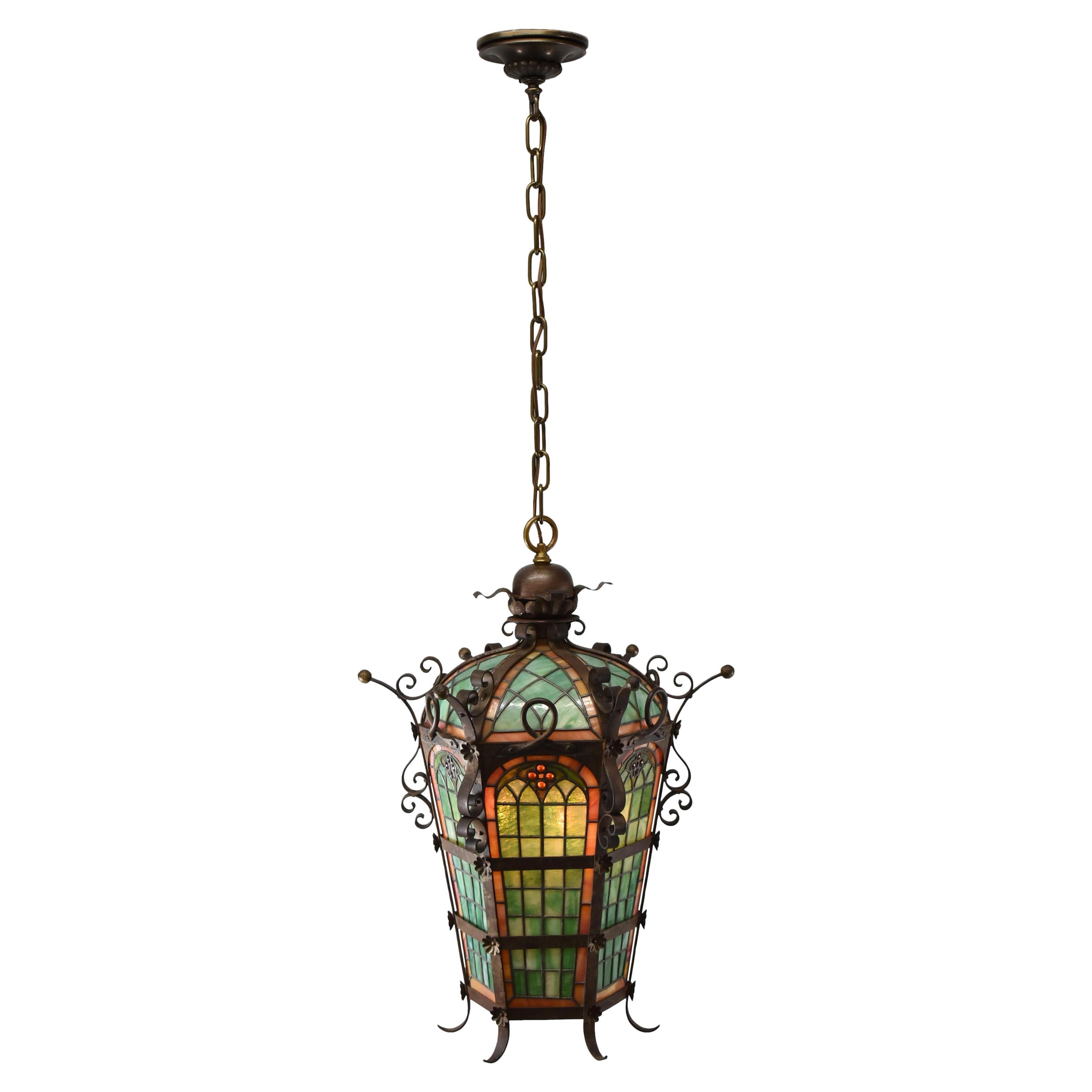 Large antique Gothic Revival leaded slag glass chandelier or pendant. Heavy granite back glass in green and melon. Applied metalwork floral details. Faceted jewels.