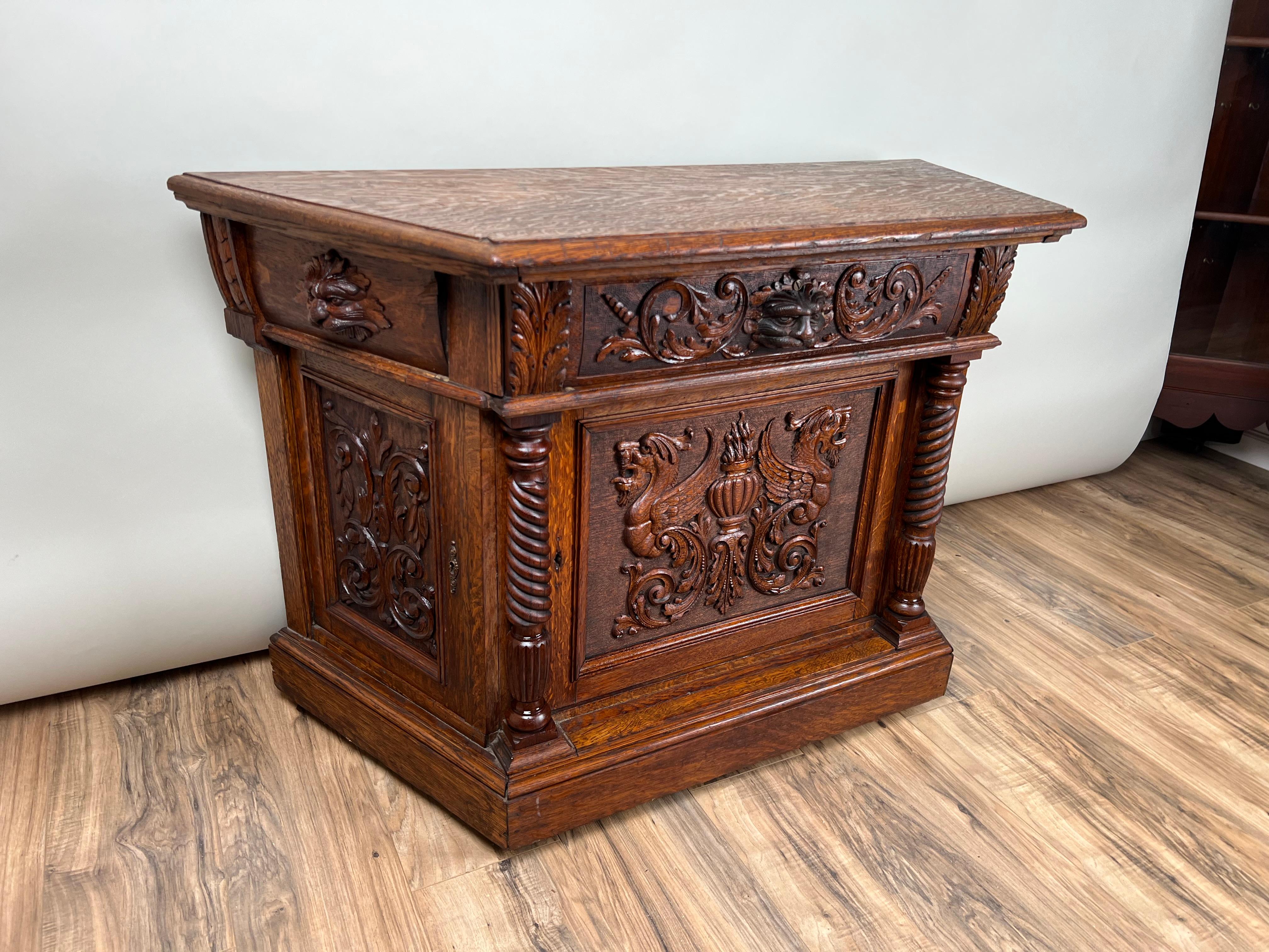 Este Antiguo Gabinete de Hombre Verde de Roble Tigre del Renacimiento Gótico, de hacia 1910, muestra los elementos de diseño distintivos del movimiento del Renacimiento Gótico. Construido en rico roble tigre, el mueble presenta tallas intrincadas y