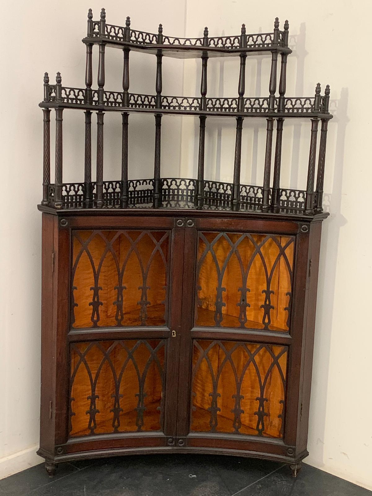 Corner cupboard with riser and two concave openwork doors with Gothic arches in the base. The ebony veneer top has an elevation with shaped shelves, finely carved rosewood columns and openwork arched railing. Maple veneered interior. Neo-Gothic