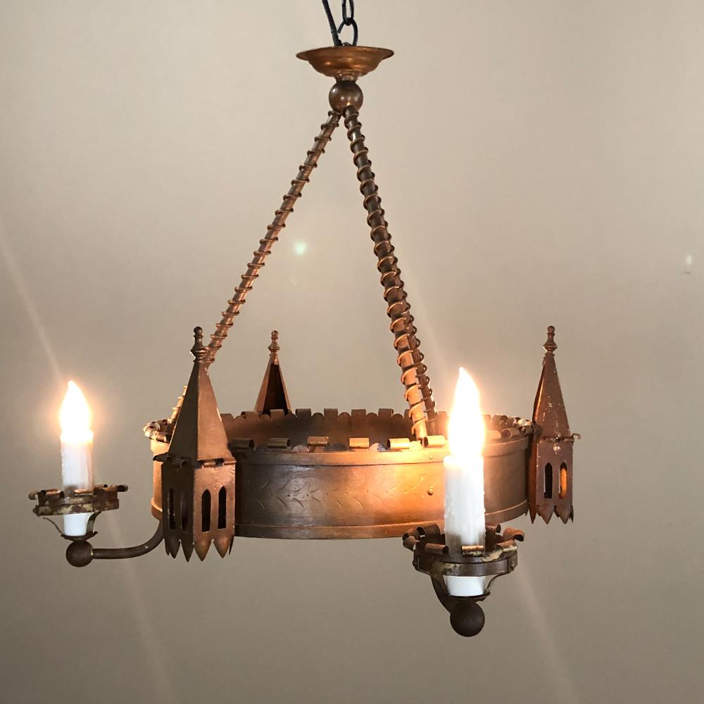 Le lustre gothique ancien en fer forgé donne un air rustique tout en étant charmant avec ses parapets montés entre les bras qui maintiennent les lumières avec leurs lobes crénelés. Le baldaquin original est conçu pour être fixé au plafond, ce qui en