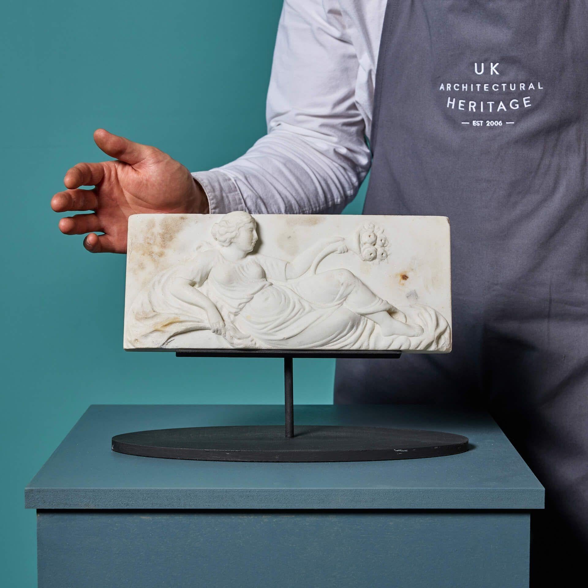 Un'antica targa in marmo statuario bianco intagliato in stile Grand Tour.

Risalente al 1830 circa, questa elegante tavoletta raffigura una scena neoclassica sapientemente intagliata a mano.

Una donna reclinata su eleganti drappi, in abito