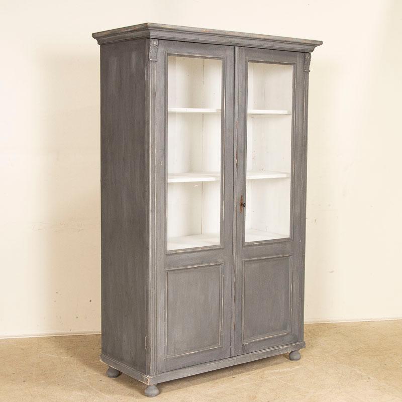 The glass panels in the front doors make this bookcase an ideal display cabinet for china or other collectibles. While the pine cabinet is old, the newer dark gray paint is lightly distressed befitting its age. The 3 interior shelves are removeable