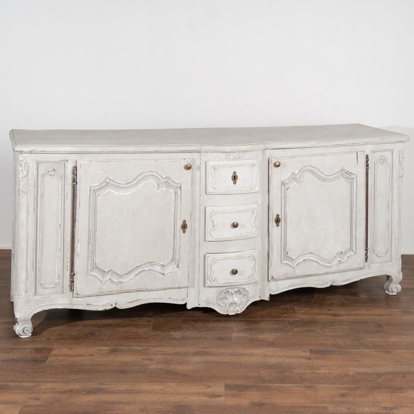 Large French oak sideboard with traditional carved panel details. At 7.5' long, this will serve as an impressive buffet resting on carved feet.
Please enlarge photos to appreciate the newer professionally applied and layered gray painted