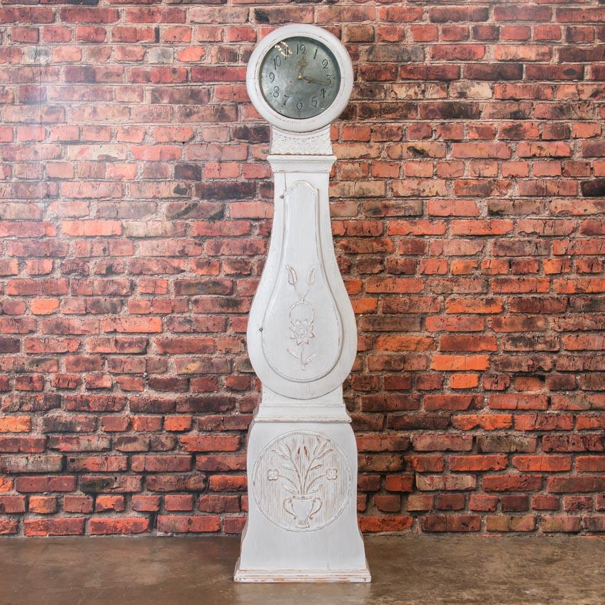 The lovely curves and perfect proportions are typical of the famous Mora grandfather clocks from Sweden. What is unusual are the hand carved floral details which makes this a special find. The light gray paint has been recently added, complimenting