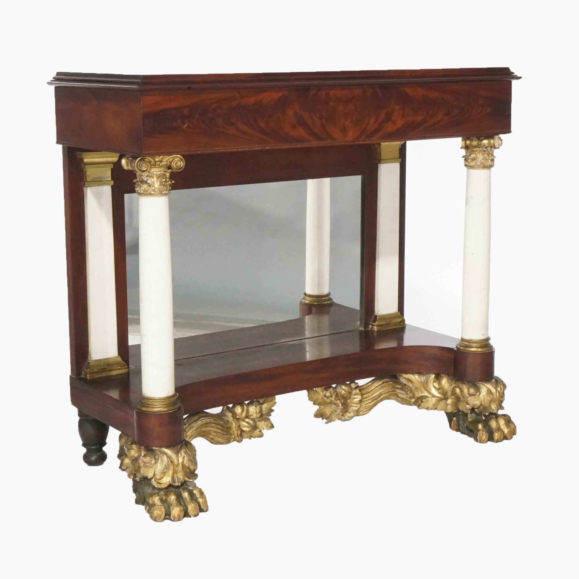 An antique American Empire Classical Greco pier table offers flame mahogany construction over base with Corinthian column marble supports having gilt capitals and mirror back, raised on gilt carved paw feet having foliate elements,