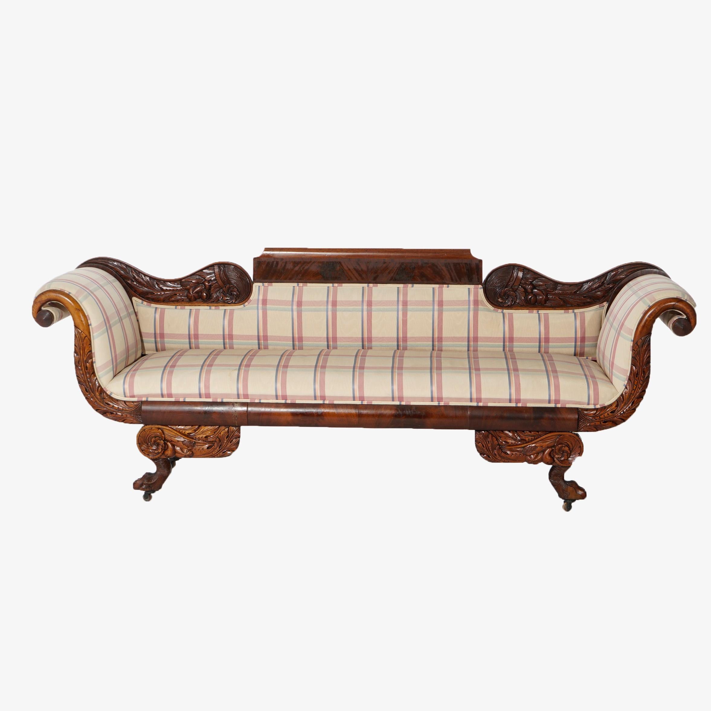 An antique Greco American Empire sofa offers flame mahogany construction with scroll form back over upholstered seat and back, scroll arms, raised on carved paw feet with foliate and floral decoration, c1840.

Measures- 35.25''H x 94''W x