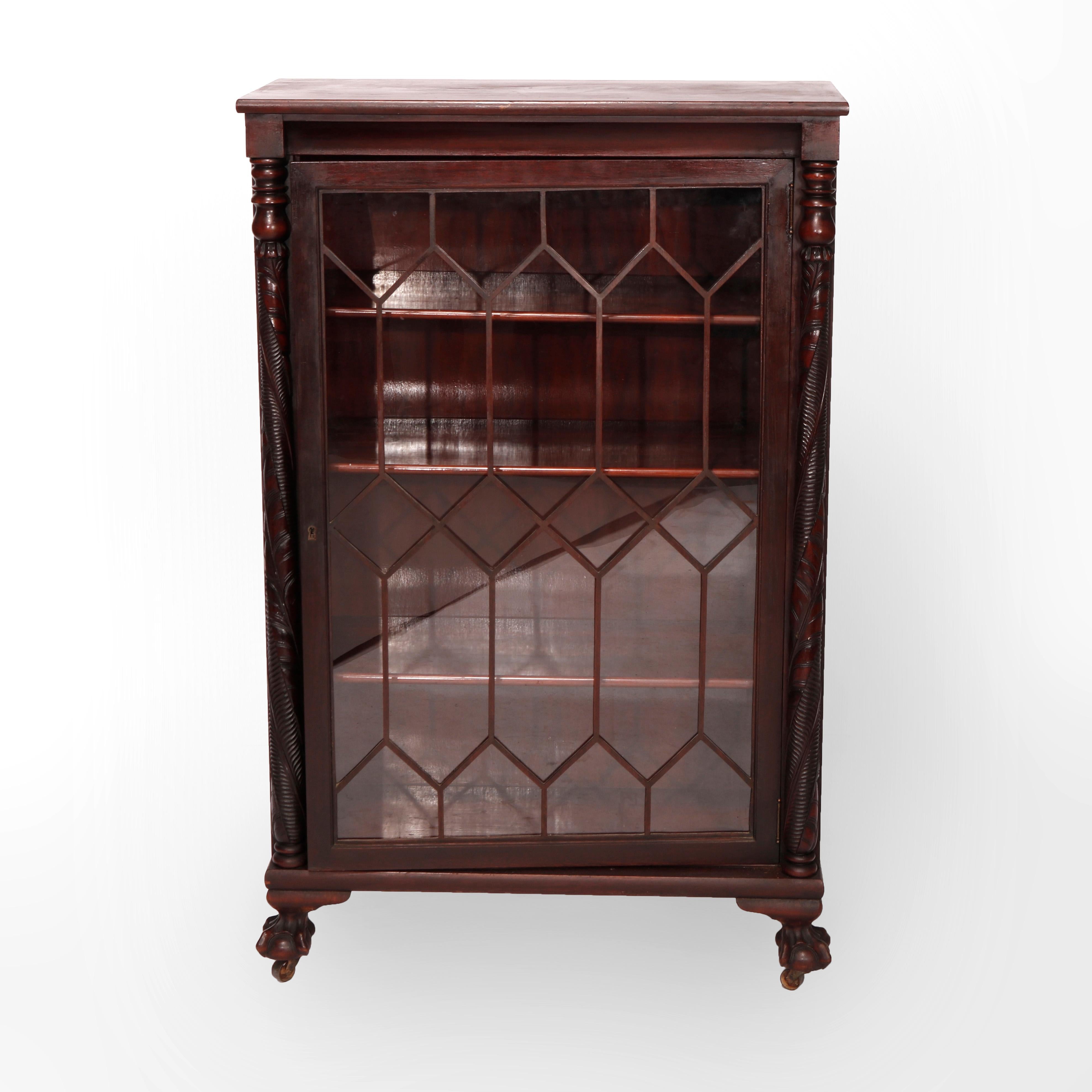 An antique American Empire bookcase with Classical Greco influence offers mahogany construction having single glass door with lattice facing and flanked by heavily carved acanthus columns, raised on carved paw feet, c1920

Measures - 49.75'' H x