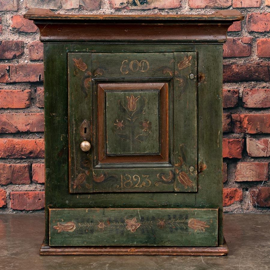 The wonderful original green paint of this delightful hanging cupboard has aged gracefully and now bears a rich patina obtained only by the passage of much time. Notice the lovely flower details, traditional for the era often portraying tulips such