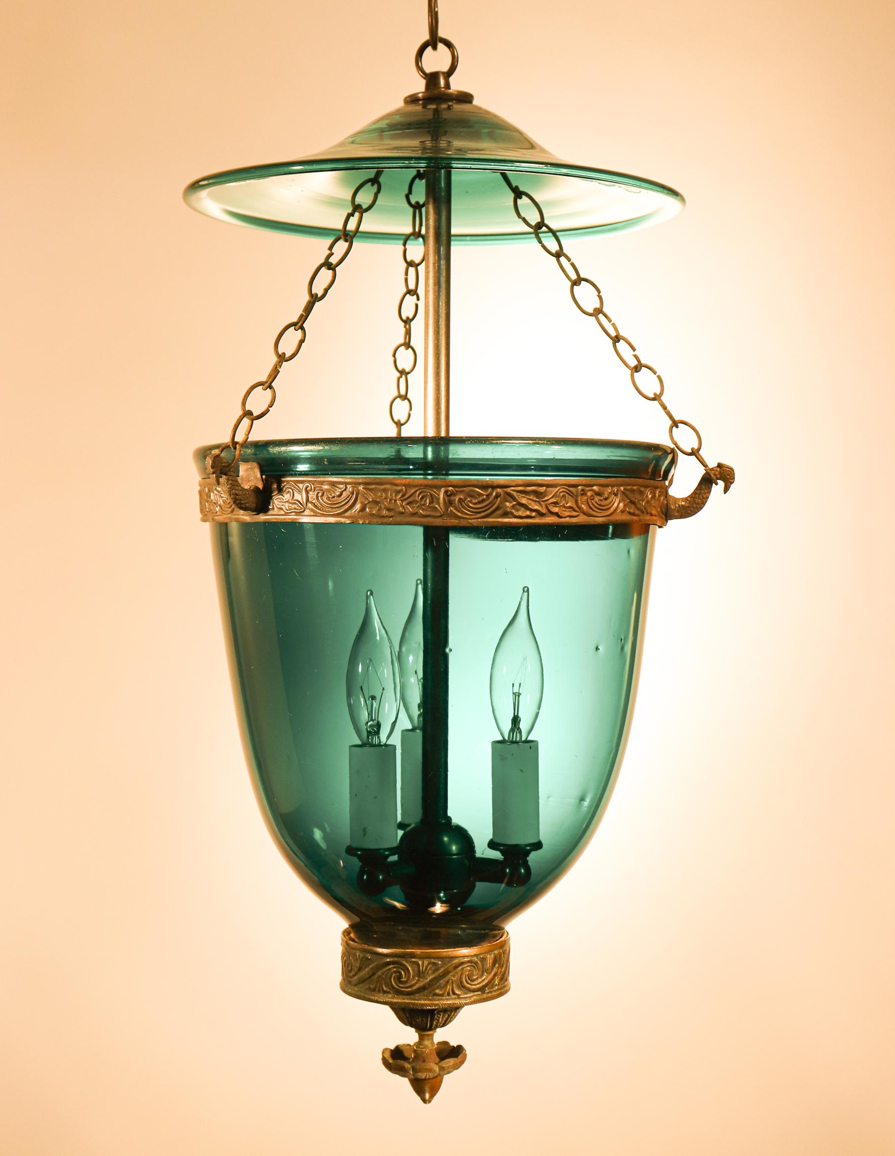 This circa 1860 English, hand blown glass bell jar lantern features a beautiful green hue and is embellished with a rare and original brass finial/candleholder base. The lantern's brass band, which has an embossed floral design, was replaced at some