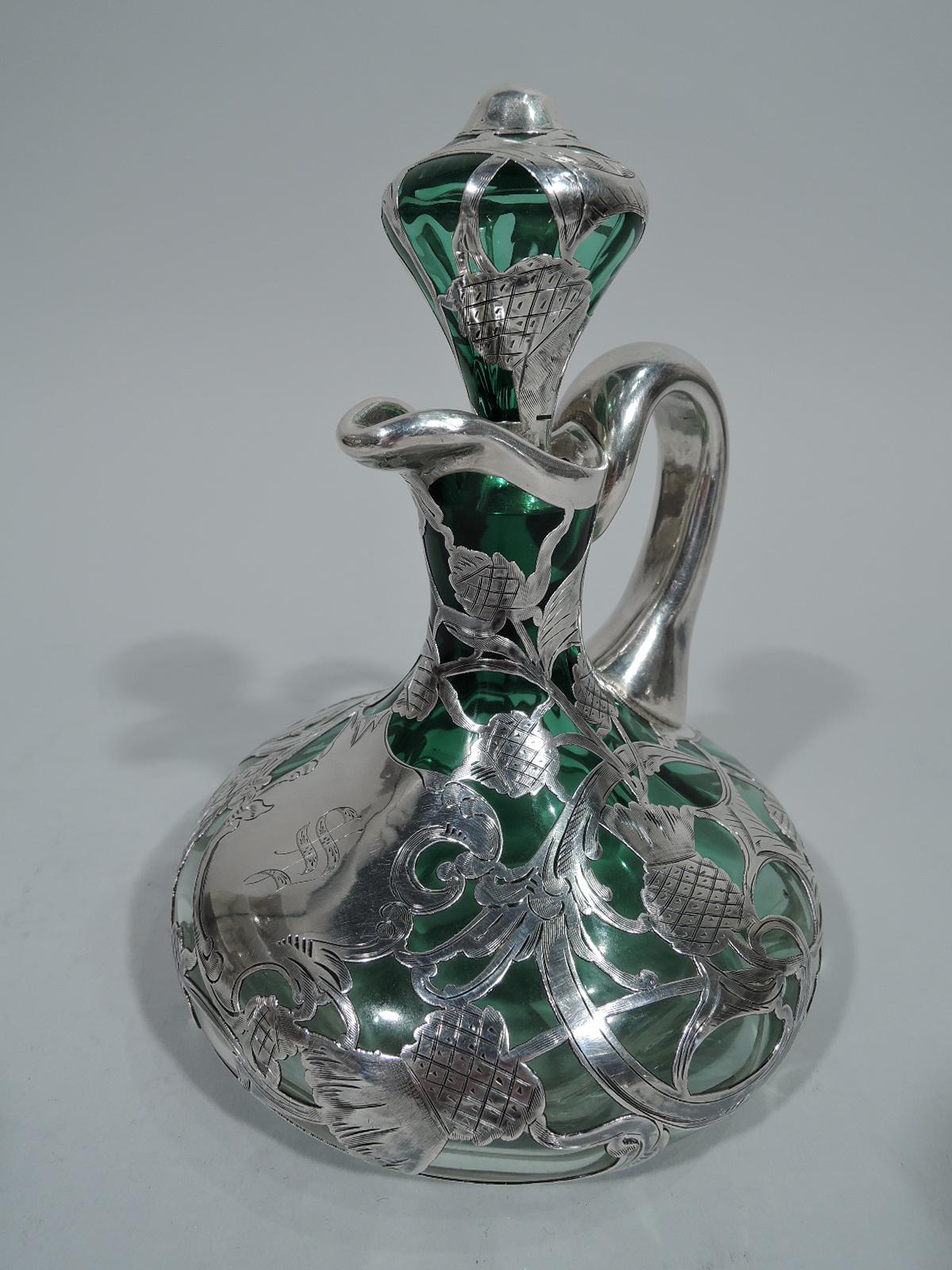 Antique glass decanter with silver overlay, circa 1900. Bellied with c-scroll handle, cylindrical neck, and stopper. Glass is green shading to clear. Overlay in form of wheat and rye grain heads on loosely scrolled and entwined stems. Asymmetrical