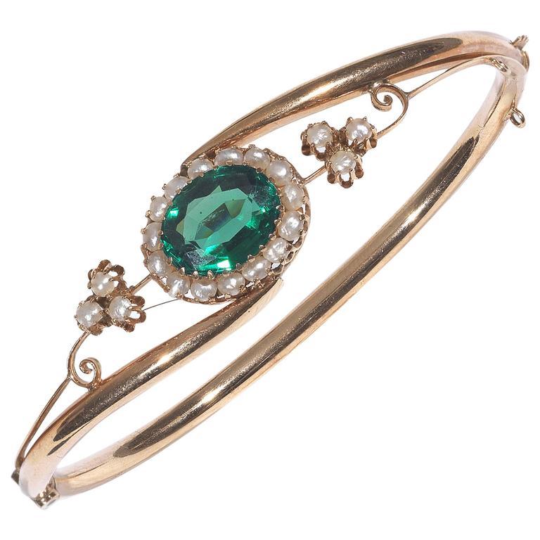 Of traditional central entwined design, centered by a claw set oval shape mixed cut green tourmaline and accented by pearls frame. 

Mounted in plain rose gold.

The bangle is hinged and opens. 

Inner diameter: 61 mm

Weight: 6.7 gr
