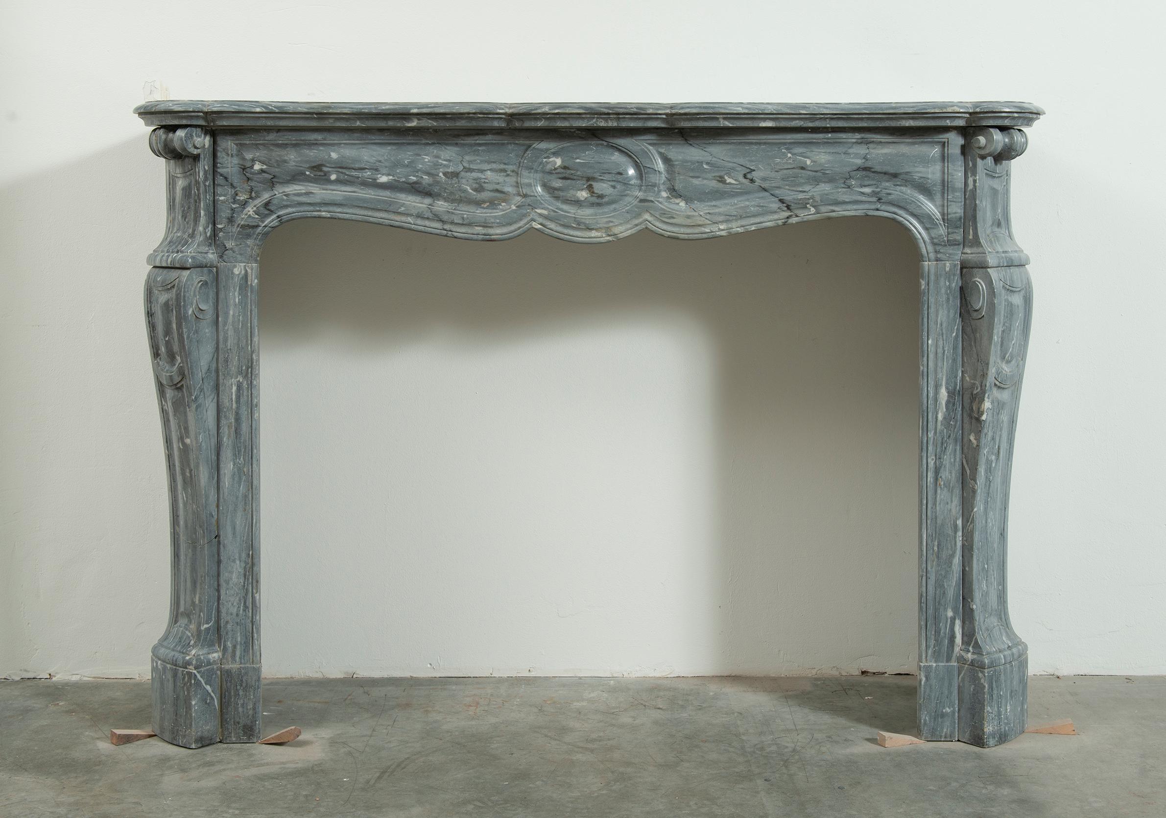 Beautiful French grey marble Louis XV style fireplace mantel.

The serpentine breakfront shelf rests above a paneled freeze centered by a large and crisp saucer echoed on the endblocks which sit above angled, paneled jambs supported on sturdy
