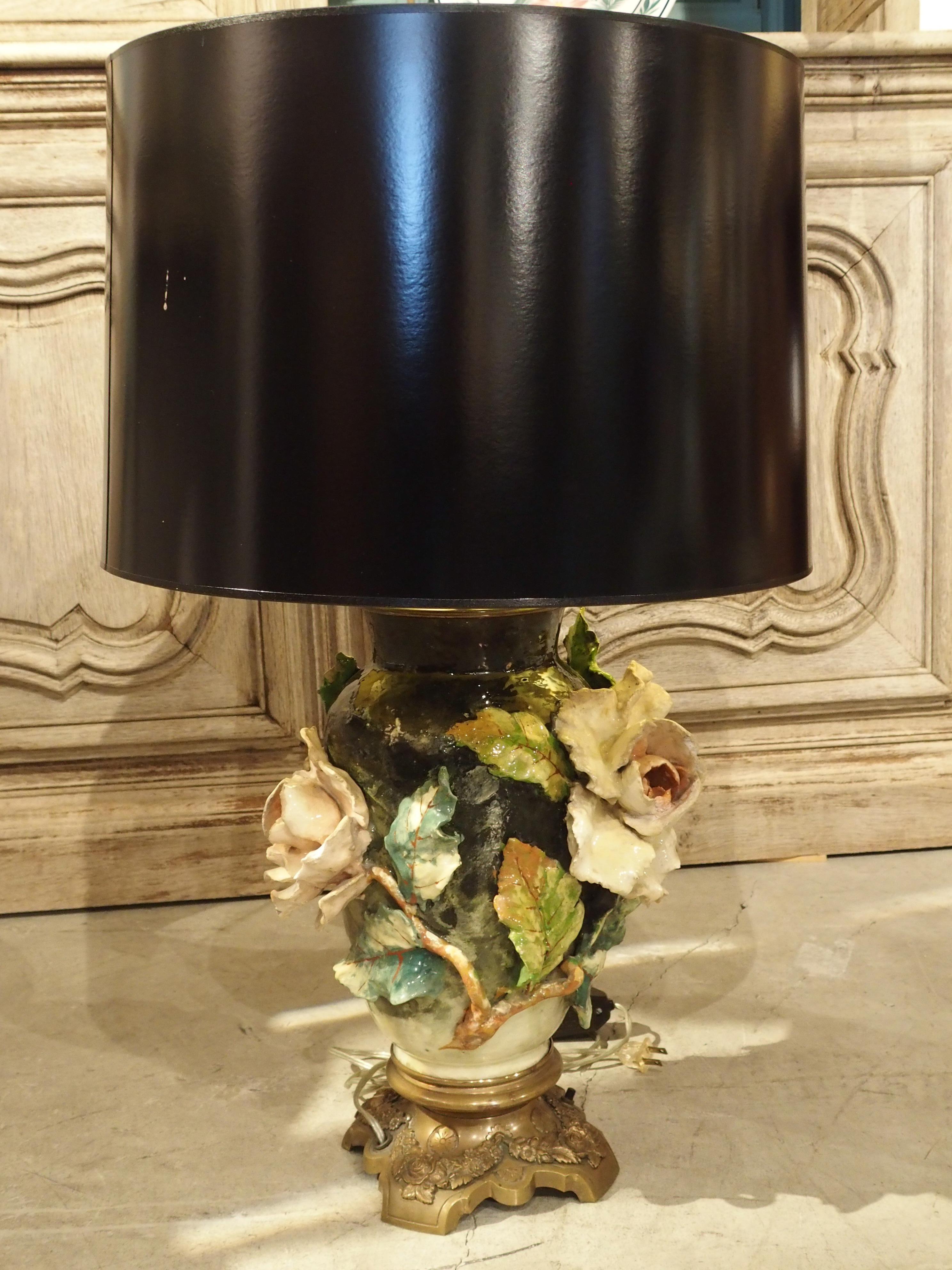 This stunning antique French lamp has been made with a barbotine vase with gross relief flowers. It is mounted to an ormolu base, and a contemporary black shade has been added. The vibrant colors of the vase include pinks, creams, greens, blacks,