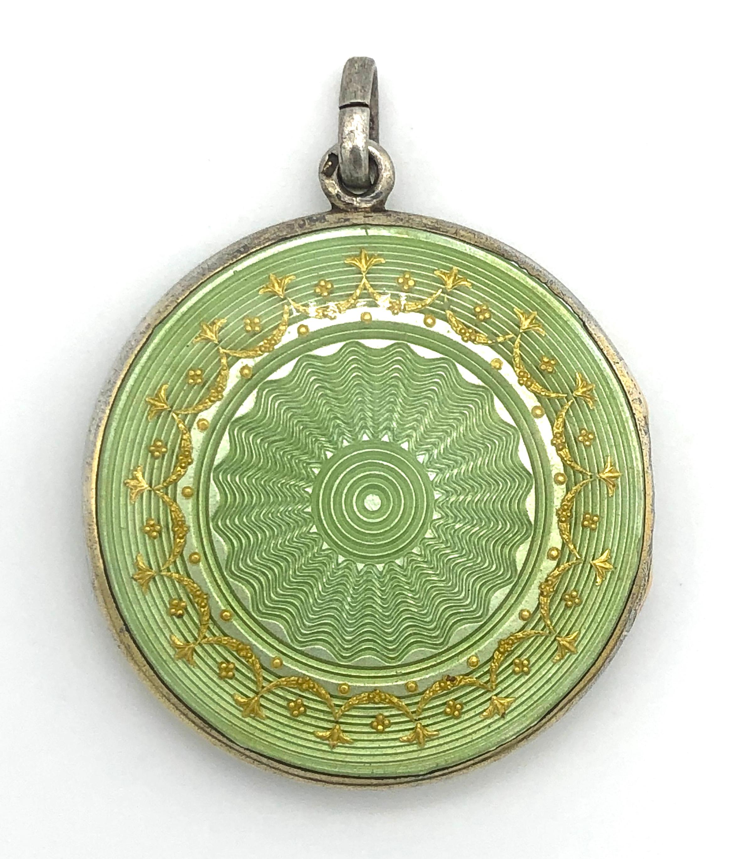 The silver locket is decorated with light green guilloché- enamel and embellished with gold enamel back and front. It is guilt on the Inside and holds the picture of a little girl.